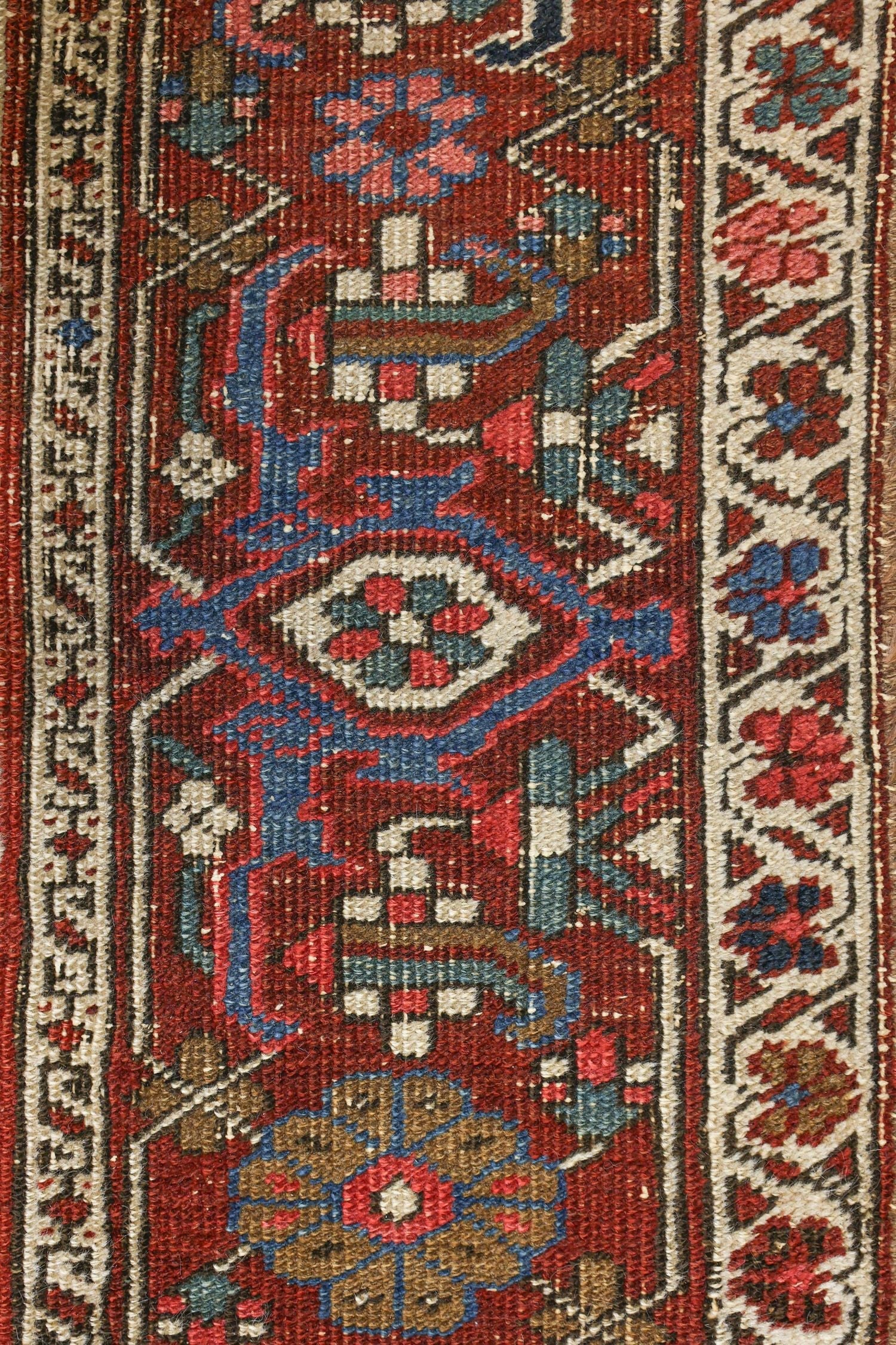 Close-up of antique Heriz rug detail, showcasing intricate handwoven pattern in red, blue, and beige.
