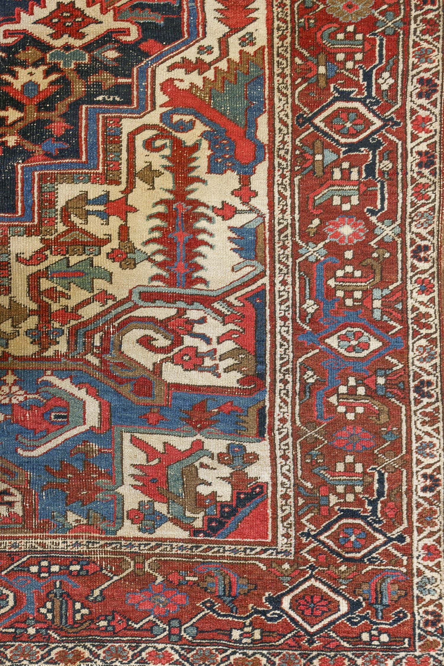 Detail of antique Heriz rug's handwoven border, showcasing intricate red, blue, and beige patterns.
