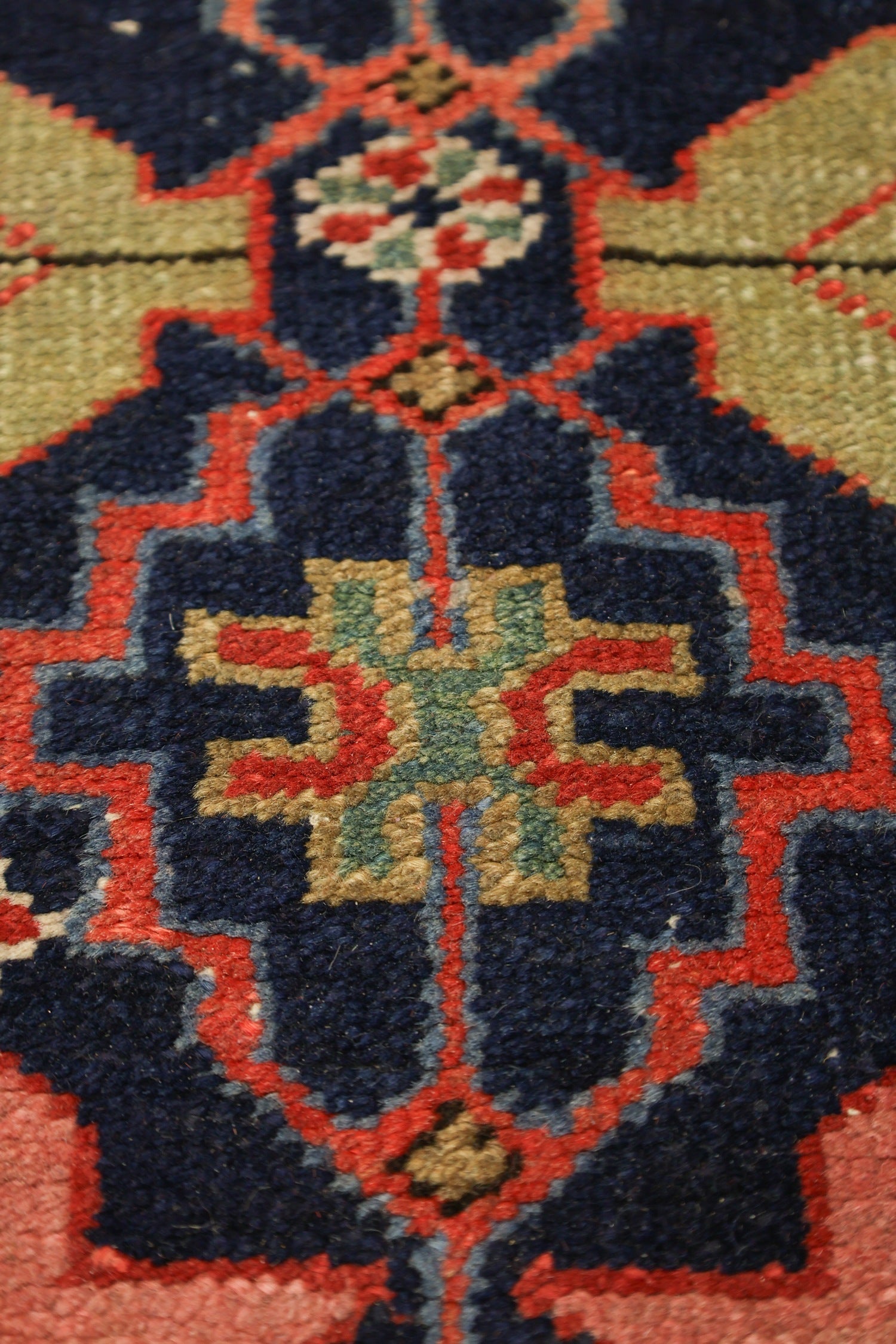 Close-up detail of a handwoven rug's intricate, colorful pattern in reds, blues, and greens.
