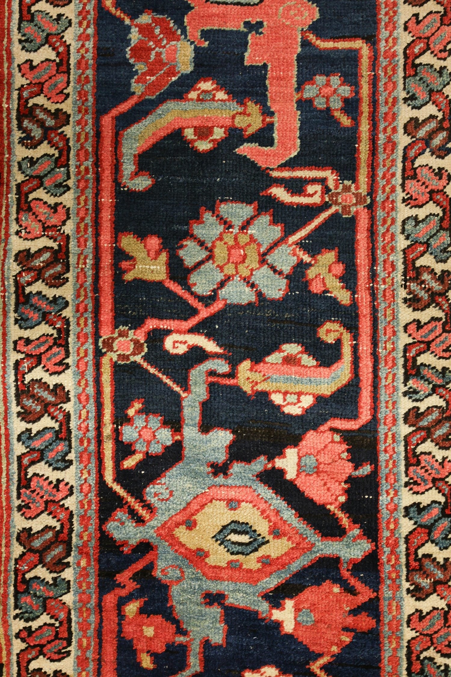 Detail of antique Heriz rug, showcasing intricate handwoven floral and geometric patterns in navy, red, and cream.
