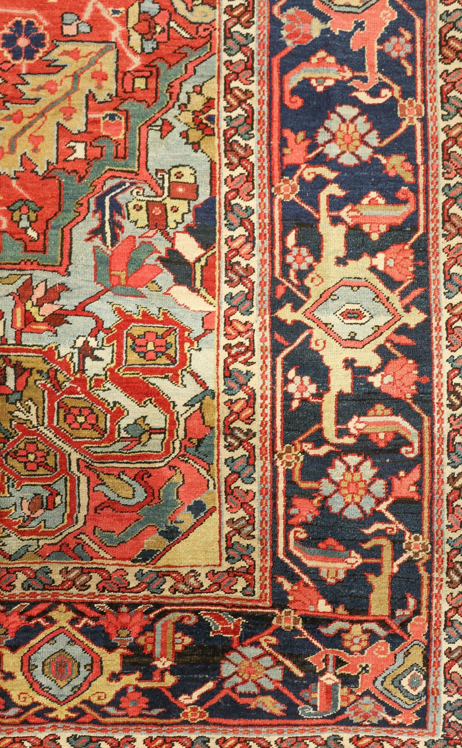 Handwoven Heriz rug detail, showcasing intricate floral and geometric patterns in red, blue, and beige.
