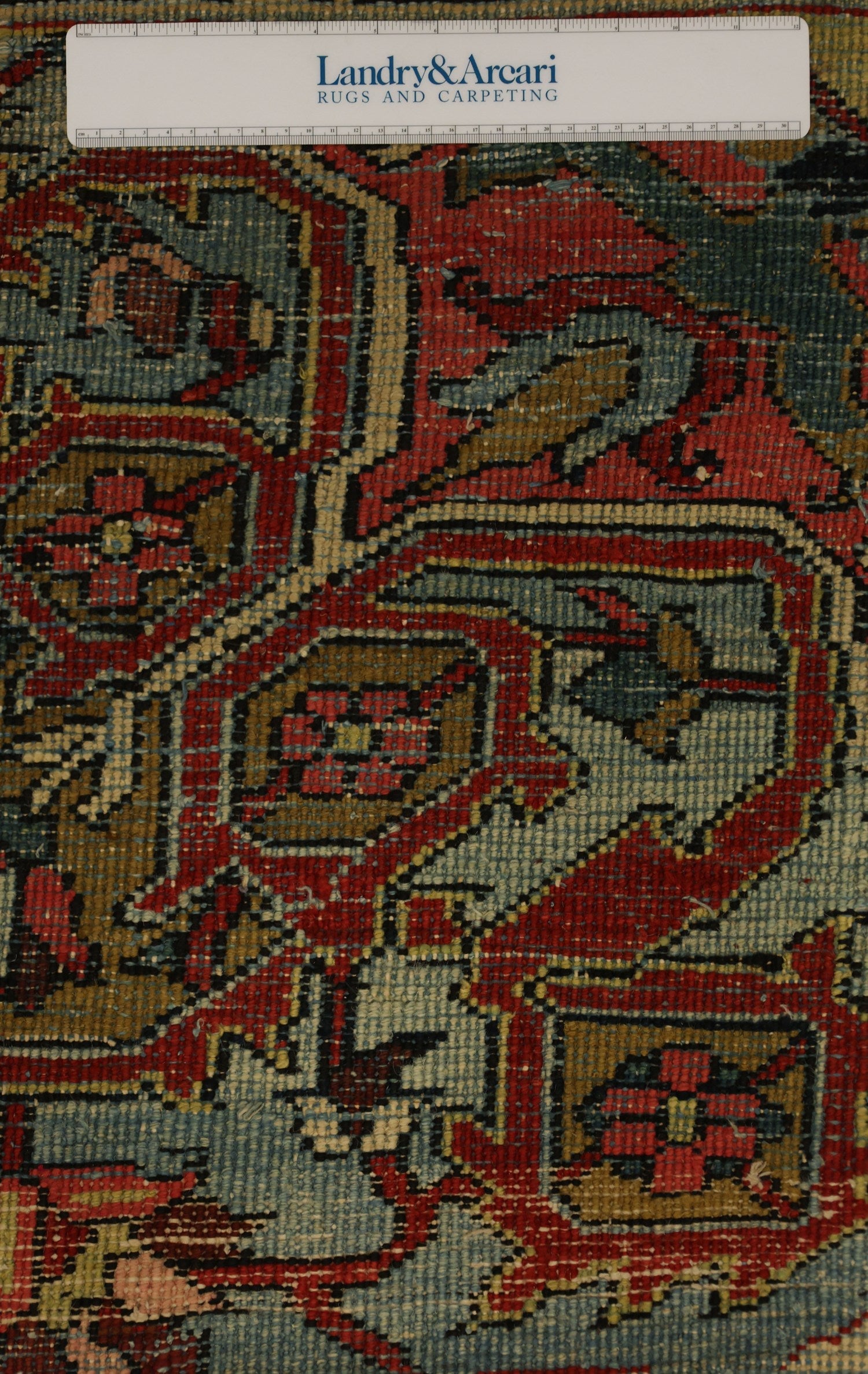 Close-up detail of antique Heriz rug's intricate, handwoven pattern in red, blue, and gold tones.
