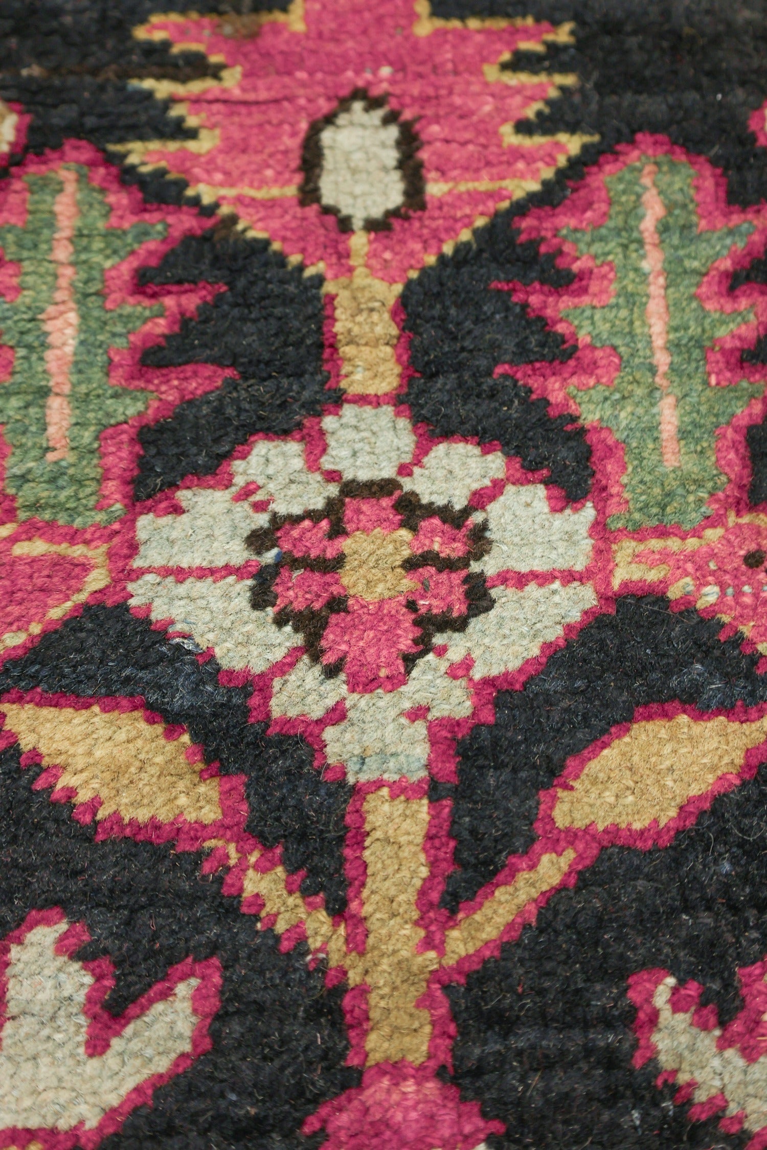 Close-up of handwoven rug detail, showcasing a pink, green, and black floral pattern.
