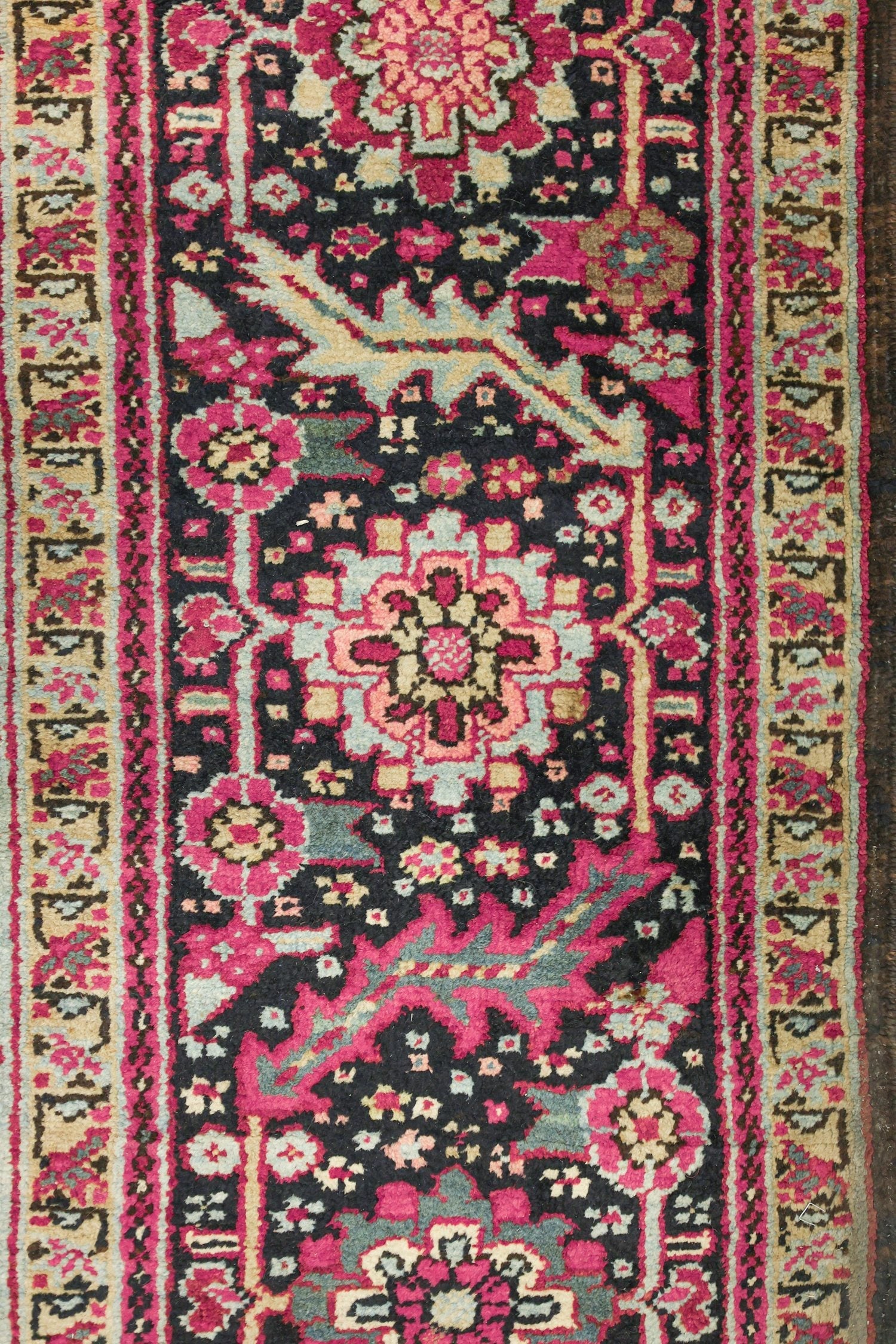 Close-up of a handwoven rug's detailed floral pattern in deep reds, pinks, and blacks.
