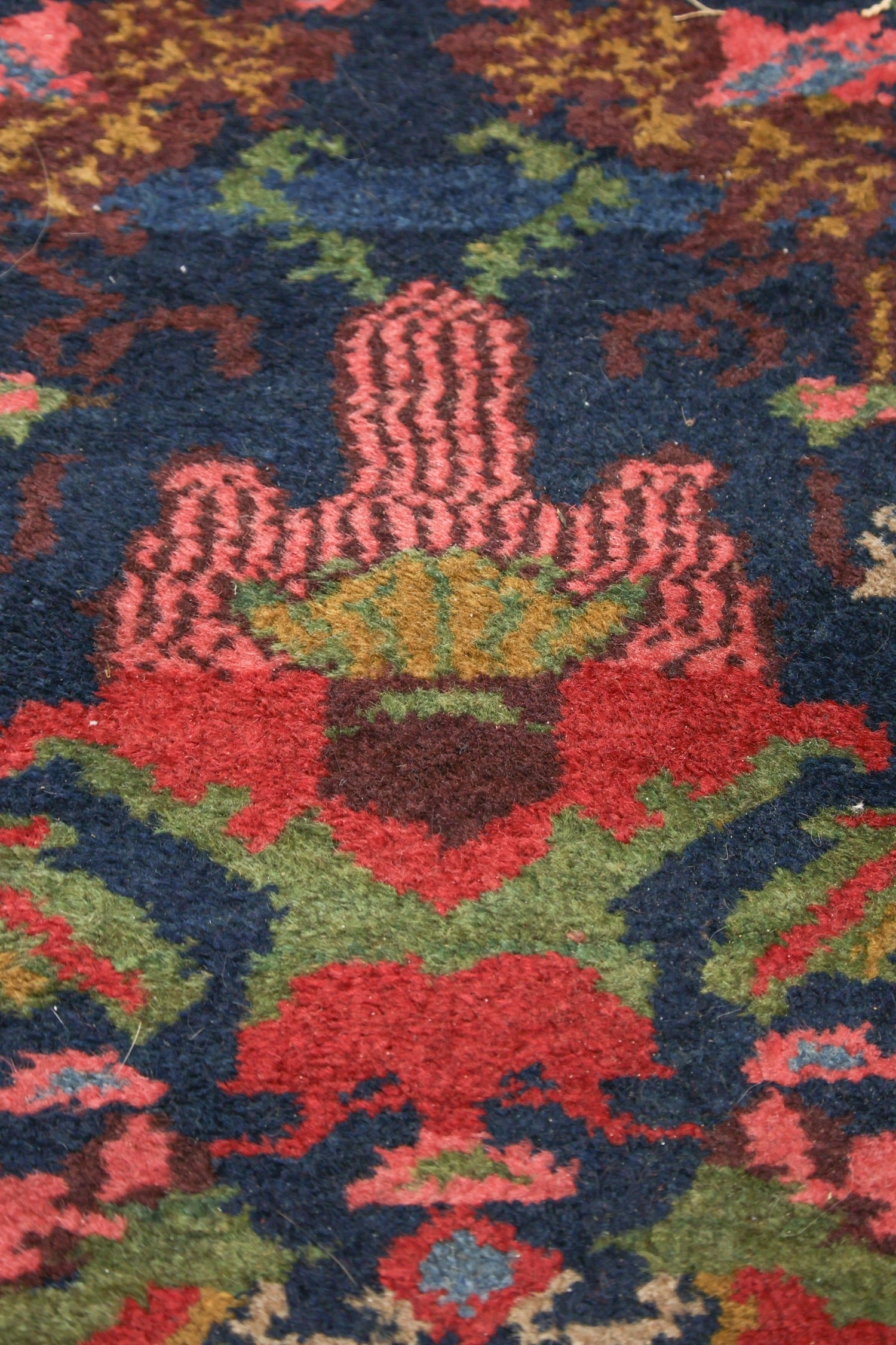 Close-up of a richly colored antique rug, showcasing handwoven details in red, green, and blue.
