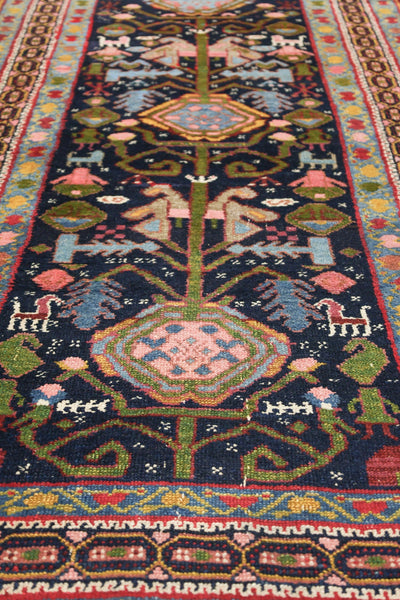 Handwoven Malayer rug detail, showcasing vibrant floral and animal motifs on a dark blue background.
