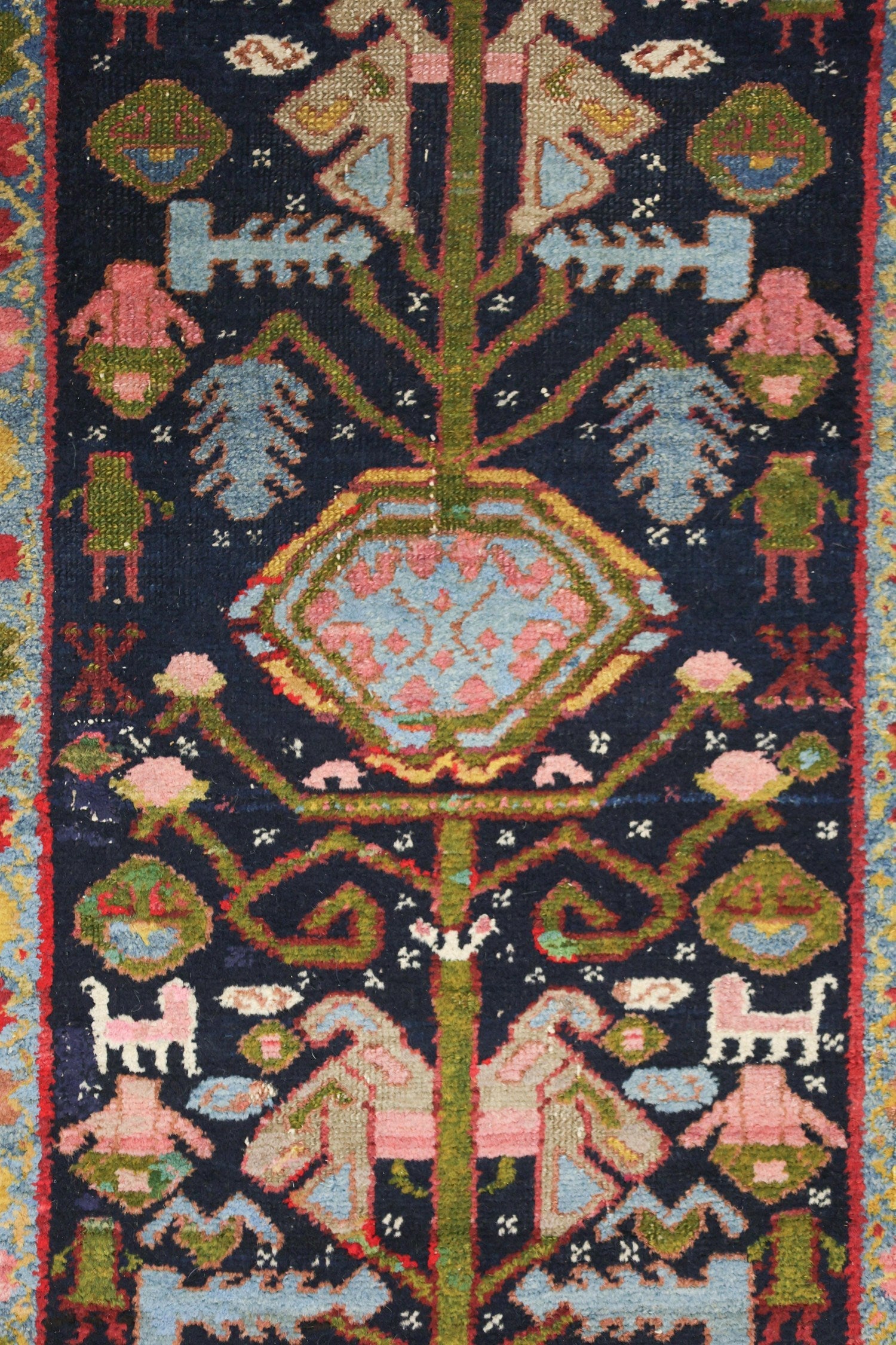 Handwoven tribal rug detail, showcasing a vibrant navy blue background with multicolored floral and animal motifs.
