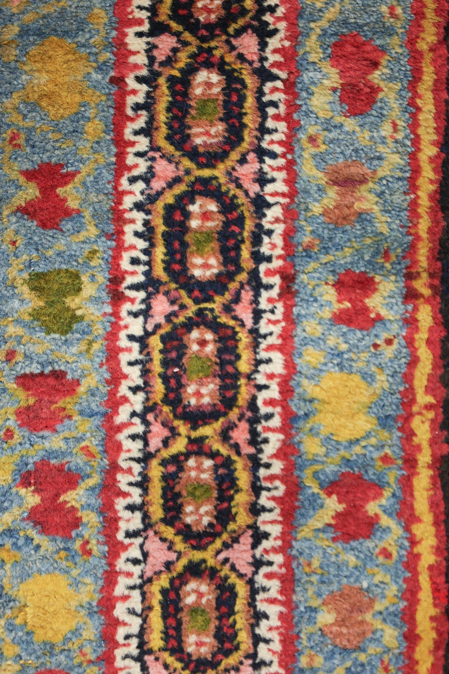 Close-up view of a handwoven rug's detailed, multicolored pattern; rich blues, reds, and yellows.
