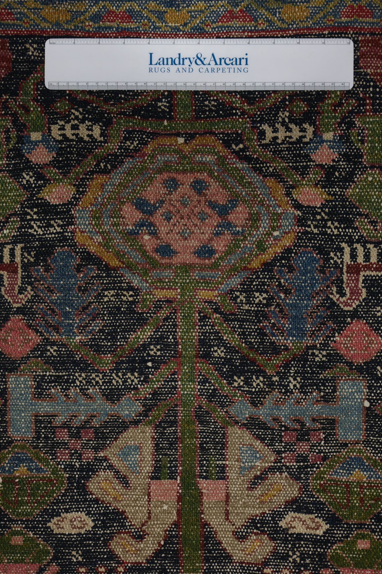 Close-up detail of antique Malayer rug's handwoven floral pattern, showcasing dark background with muted pinks and blues.
