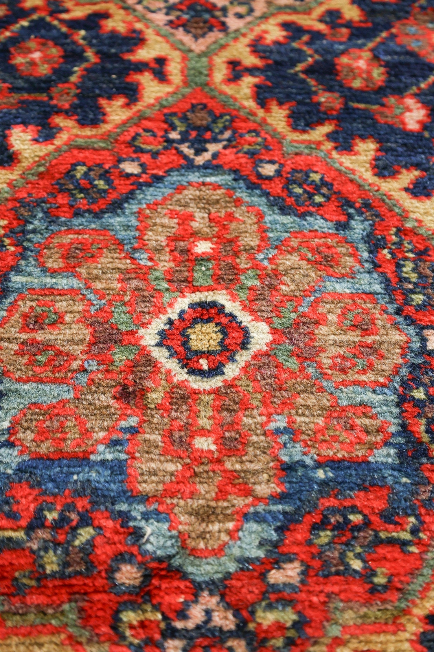 Close-up of a richly colored antique rug, showcasing intricate handwoven details in red, blue, and beige.
