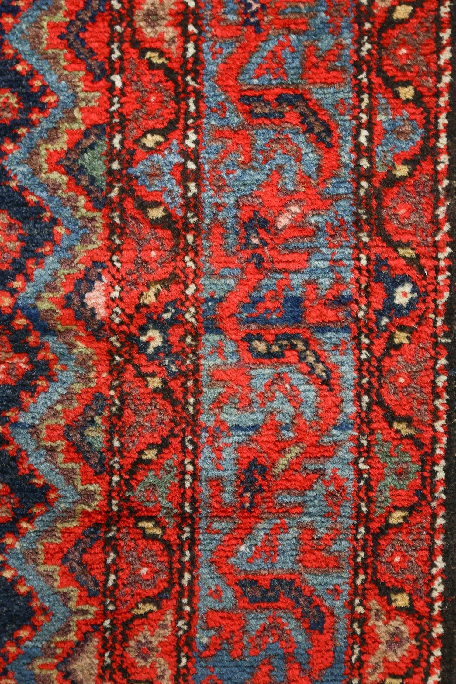 Close-up of handwoven rug detail, showcasing vibrant red and blue tones in intricate tribal pattern.
