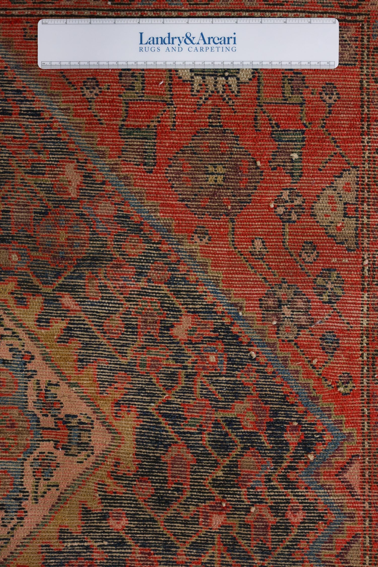 Close-up detail of an antique Malayer rug's handwoven texture, showcasing a red and navy floral pattern.
