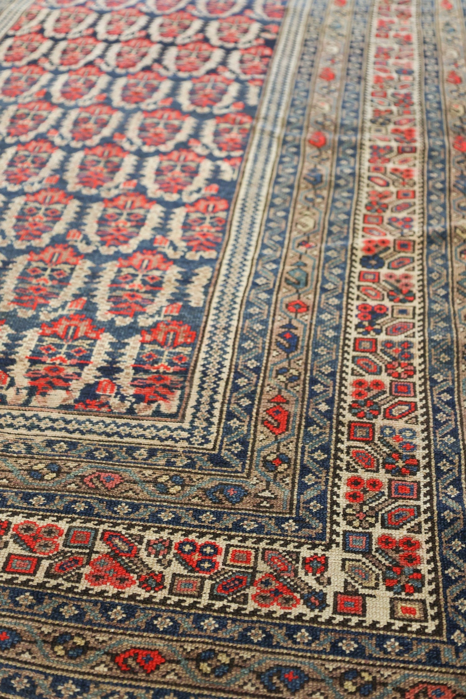 Handwoven tribal rug detail, showcasing intricate red and blue patterns on an off-white background.
