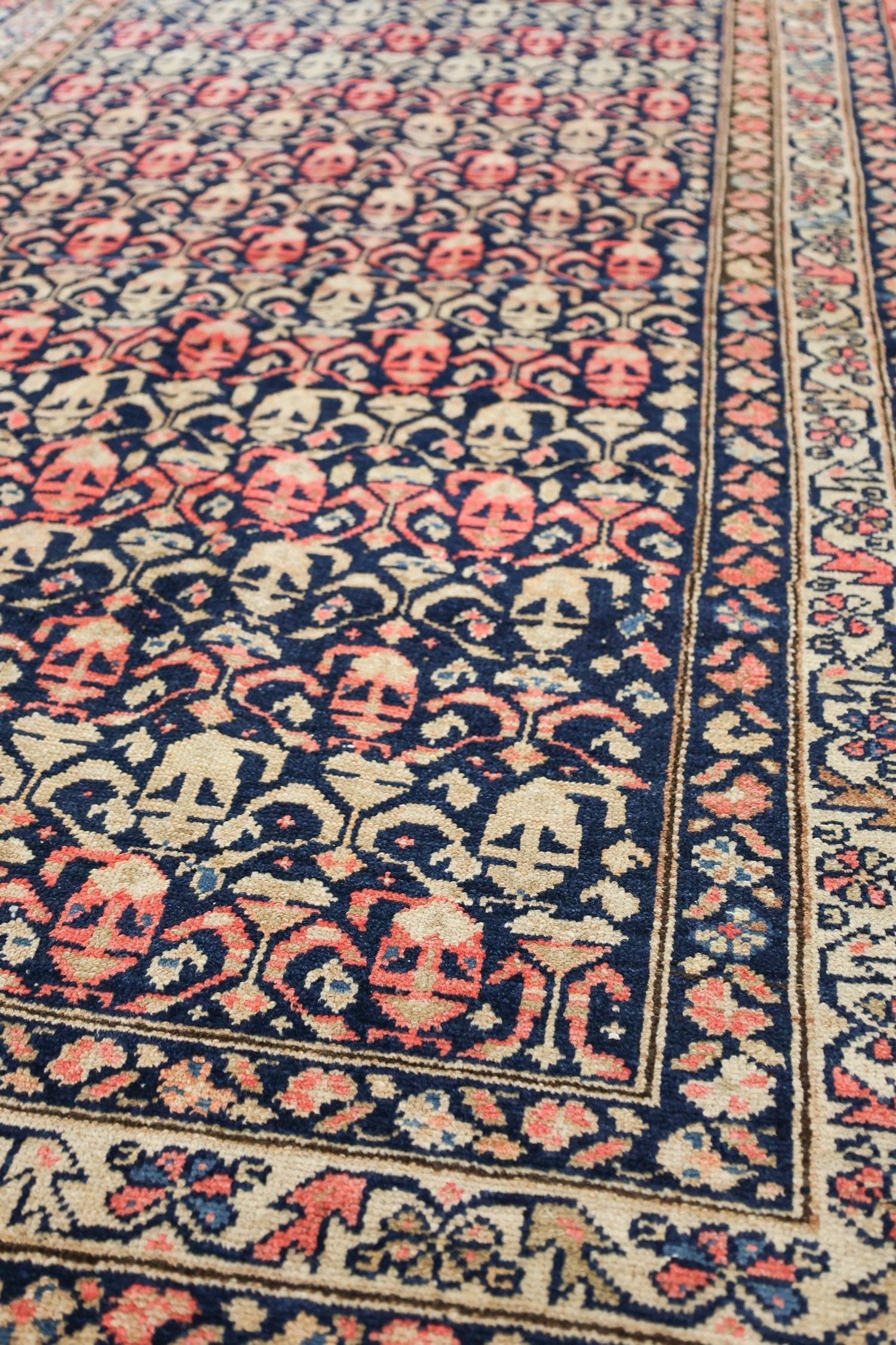 Handwoven antique Malayer rug detail, showcasing a navy, beige, and coral floral pattern.
