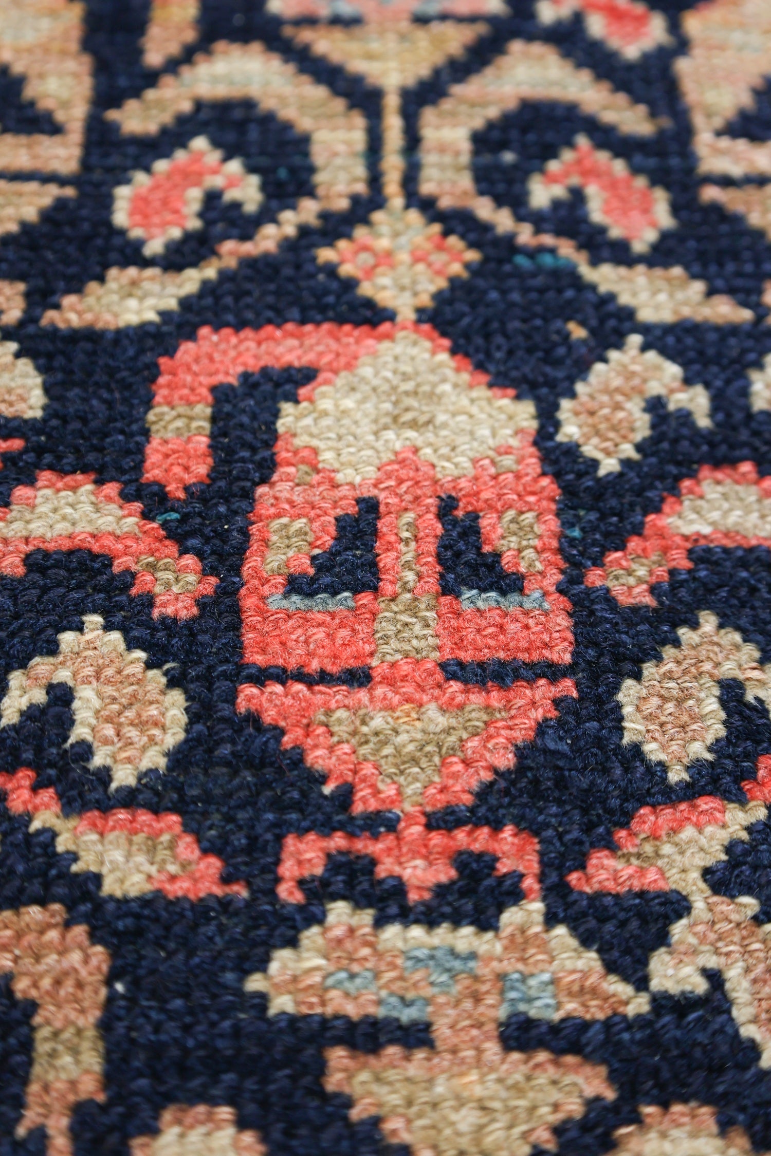 Close-up of handwoven rug detail; intricate pattern in red, beige, and navy.
