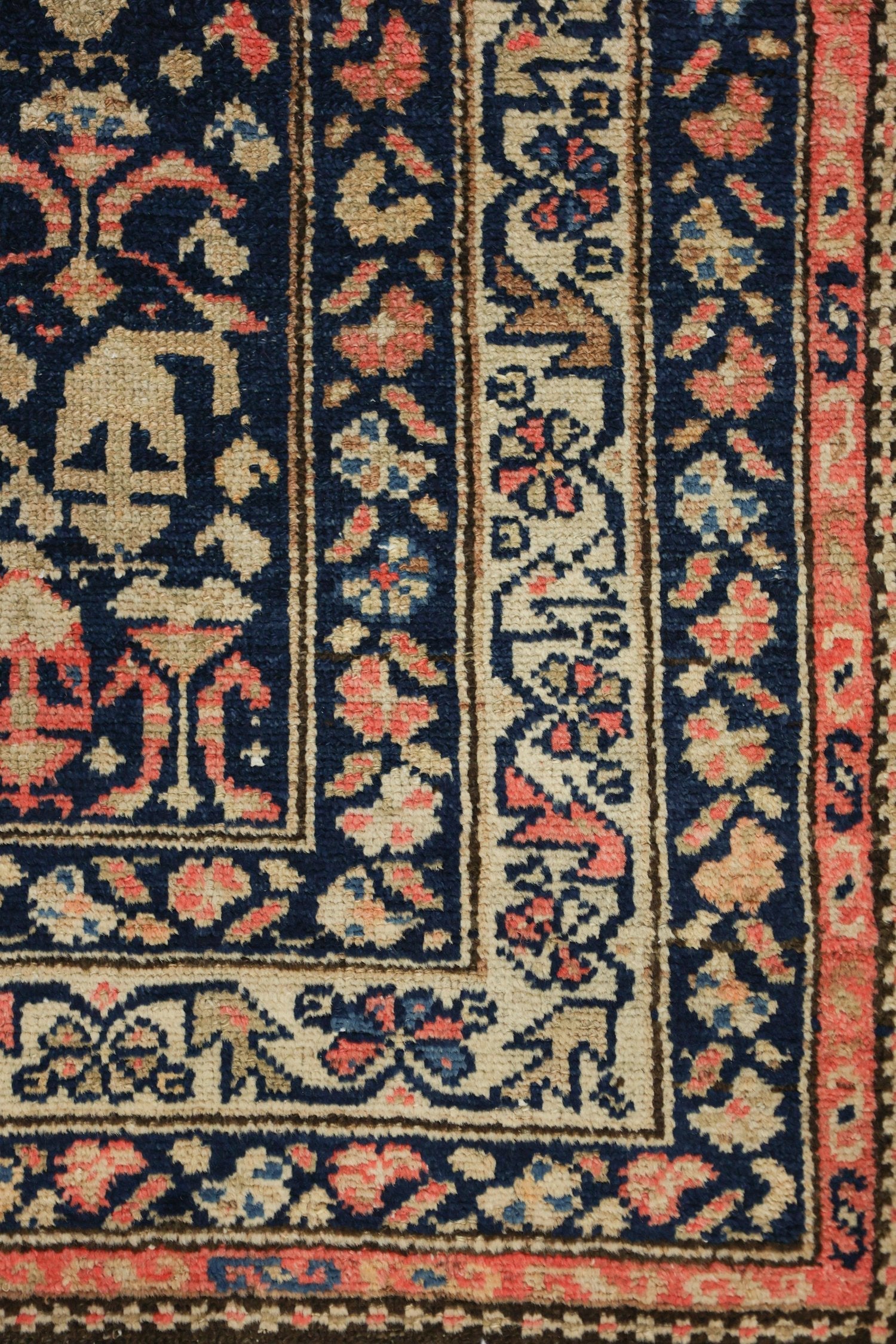 Handwoven rug detail: intricate floral and geometric patterns in beige, coral, and navy blue.
