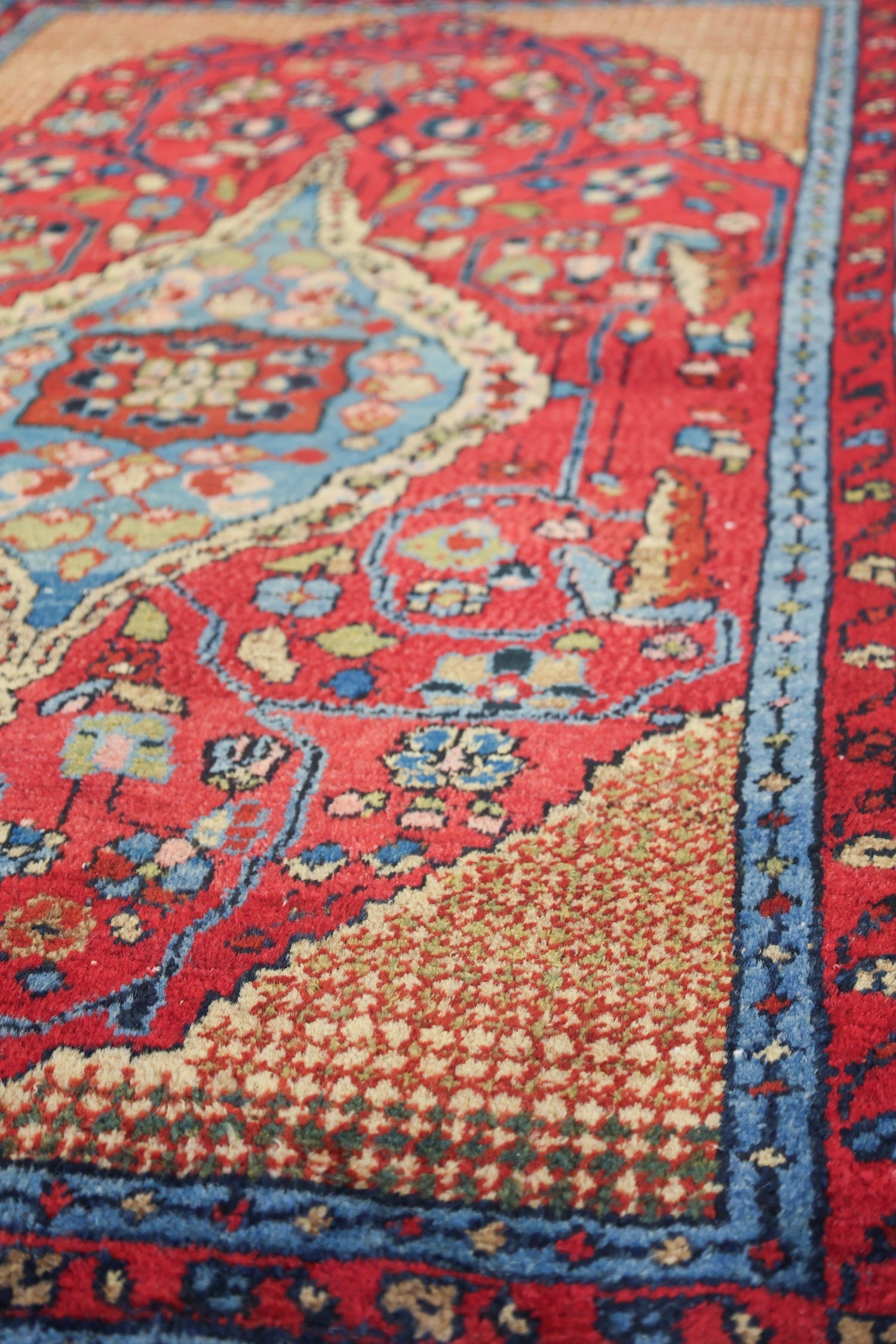 Handwoven tribal rug detail: rich red, blue, and beige tones in an intricate, antique pattern.
