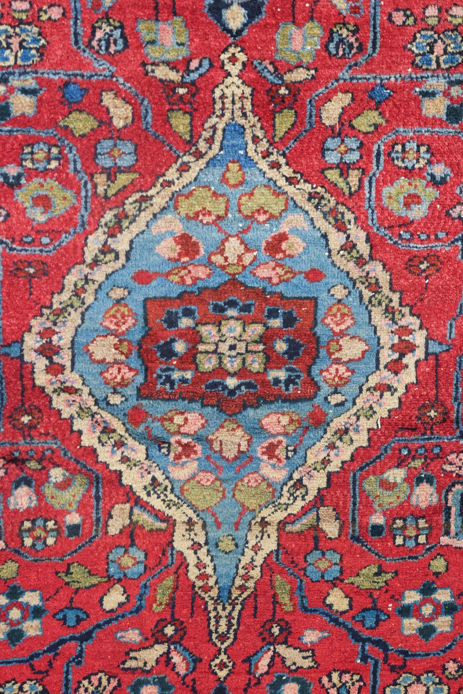 Detail of antique handwoven rug, vibrant red and blue floral pattern.
