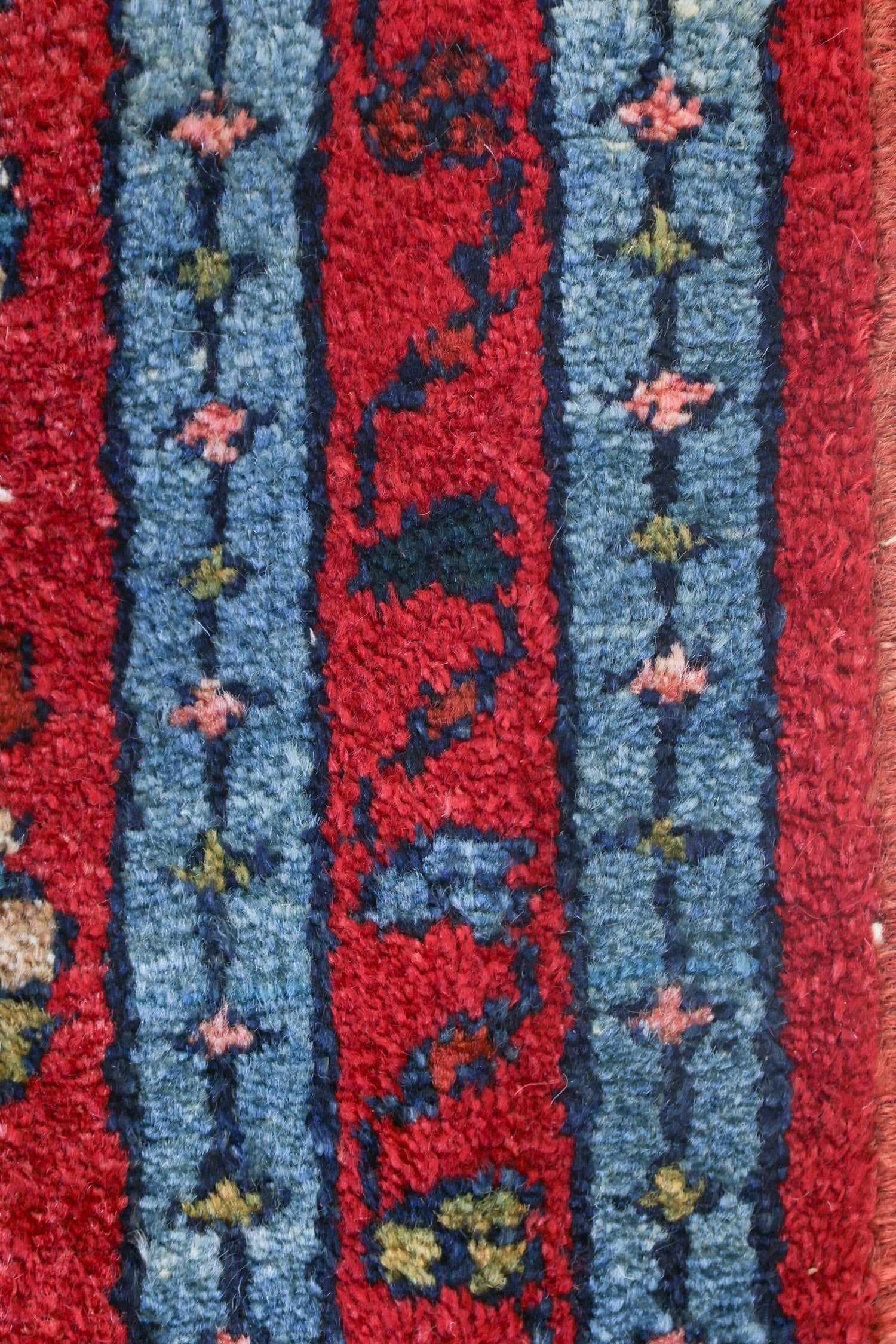 Close-up of handwoven rug detail: rich red and blue tones, intricate floral pattern.
