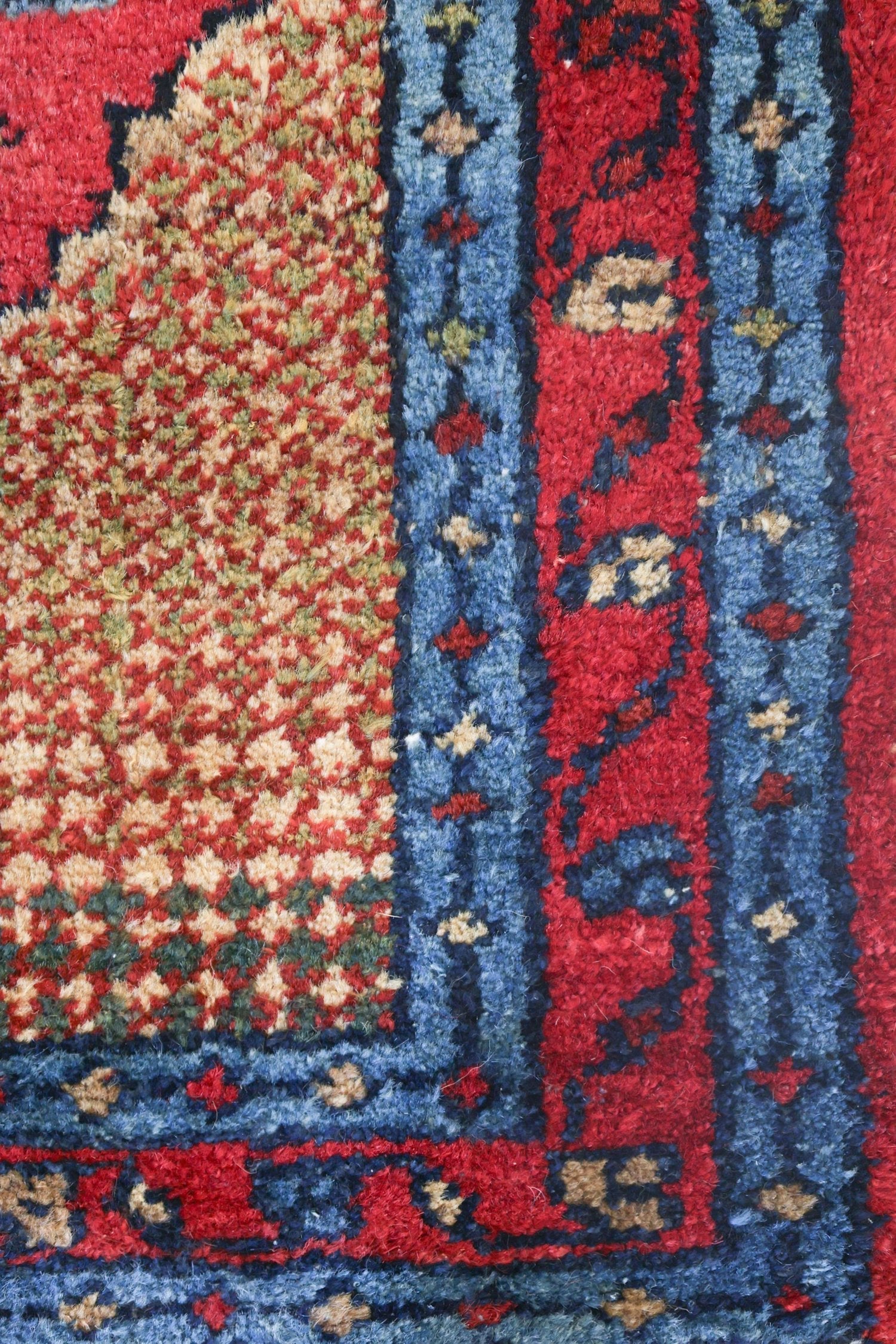 Close-up of a richly colored handwoven rug, showcasing intricate detailing in red, blue, and beige.
