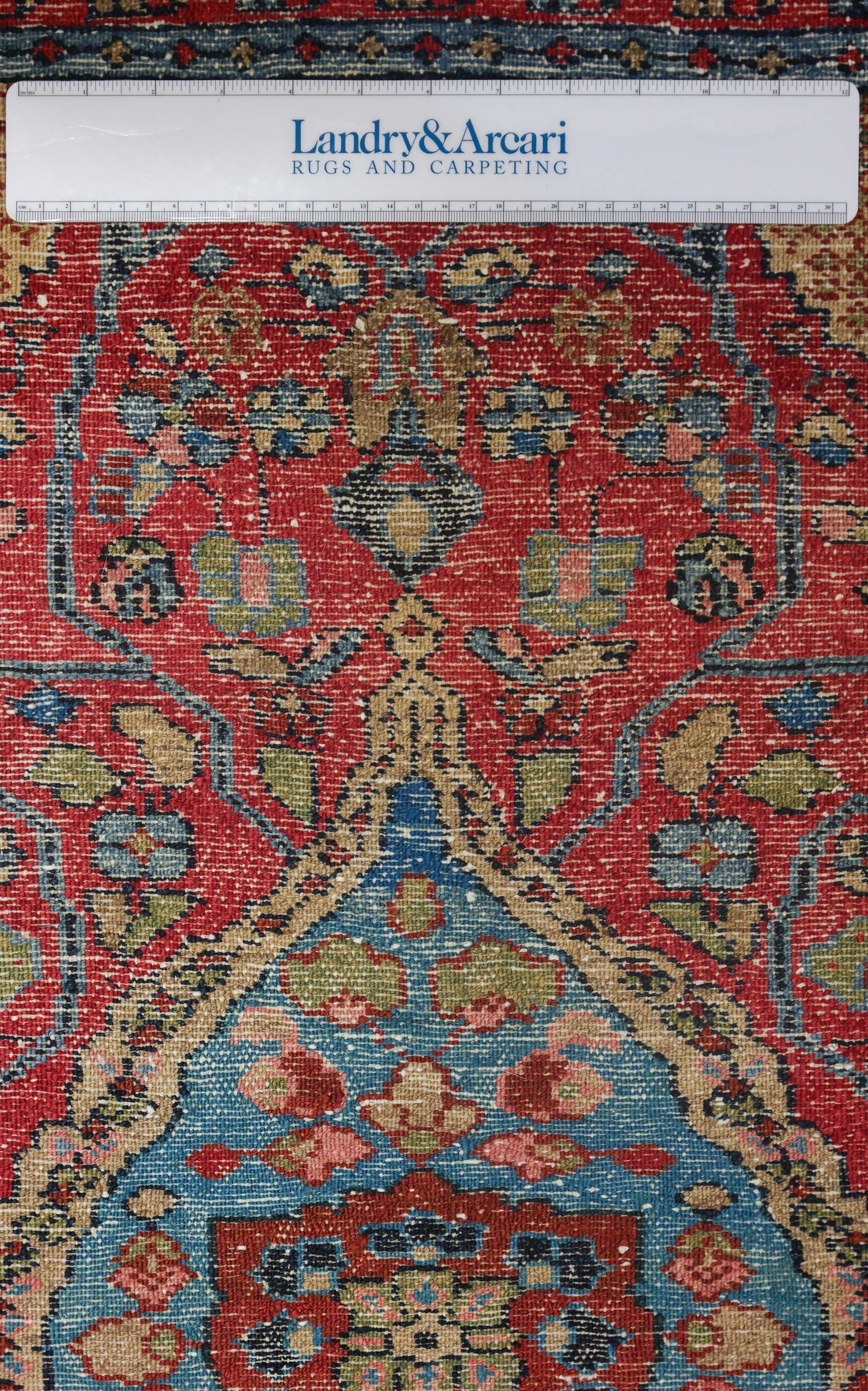 Detailed close-up of antique handwoven rug, showcasing intricate floral pattern in red, blue, and beige.
