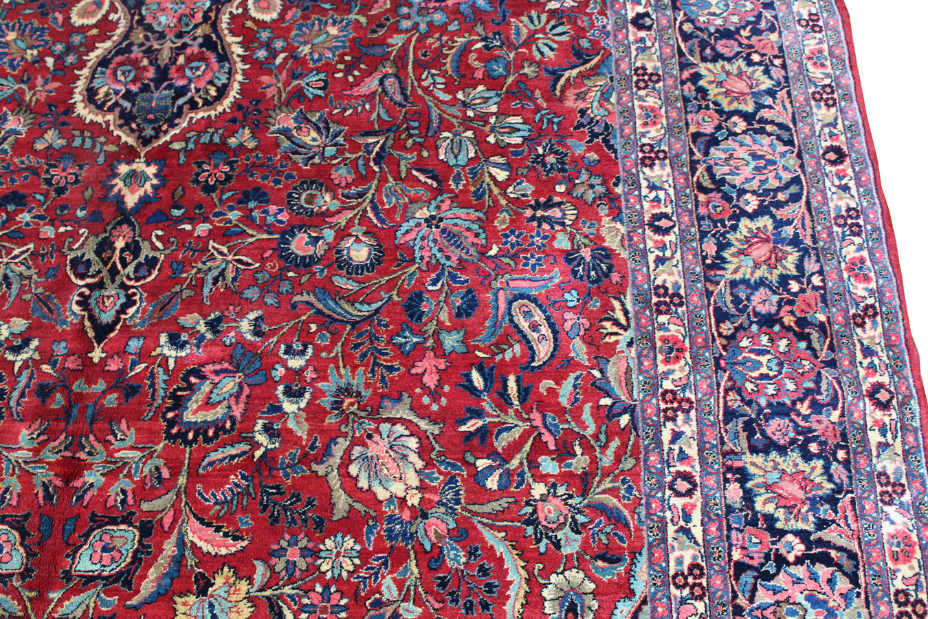 Antique handwoven rug detail: vibrant red field with intricate floral and paisley patterns in navy, teal, and cream.
