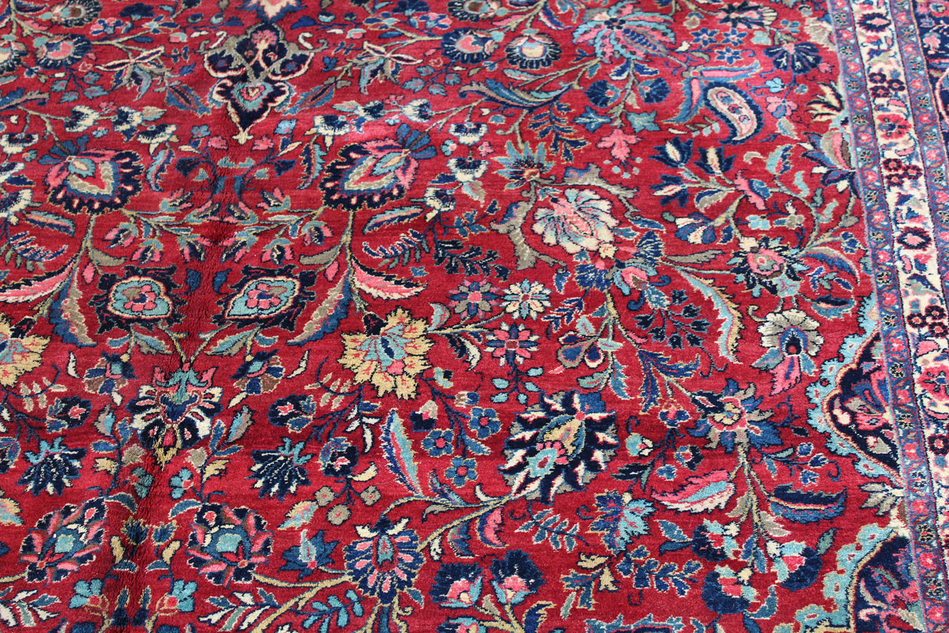 Red handwoven rug detail, intricate floral pattern in blue and cream.
