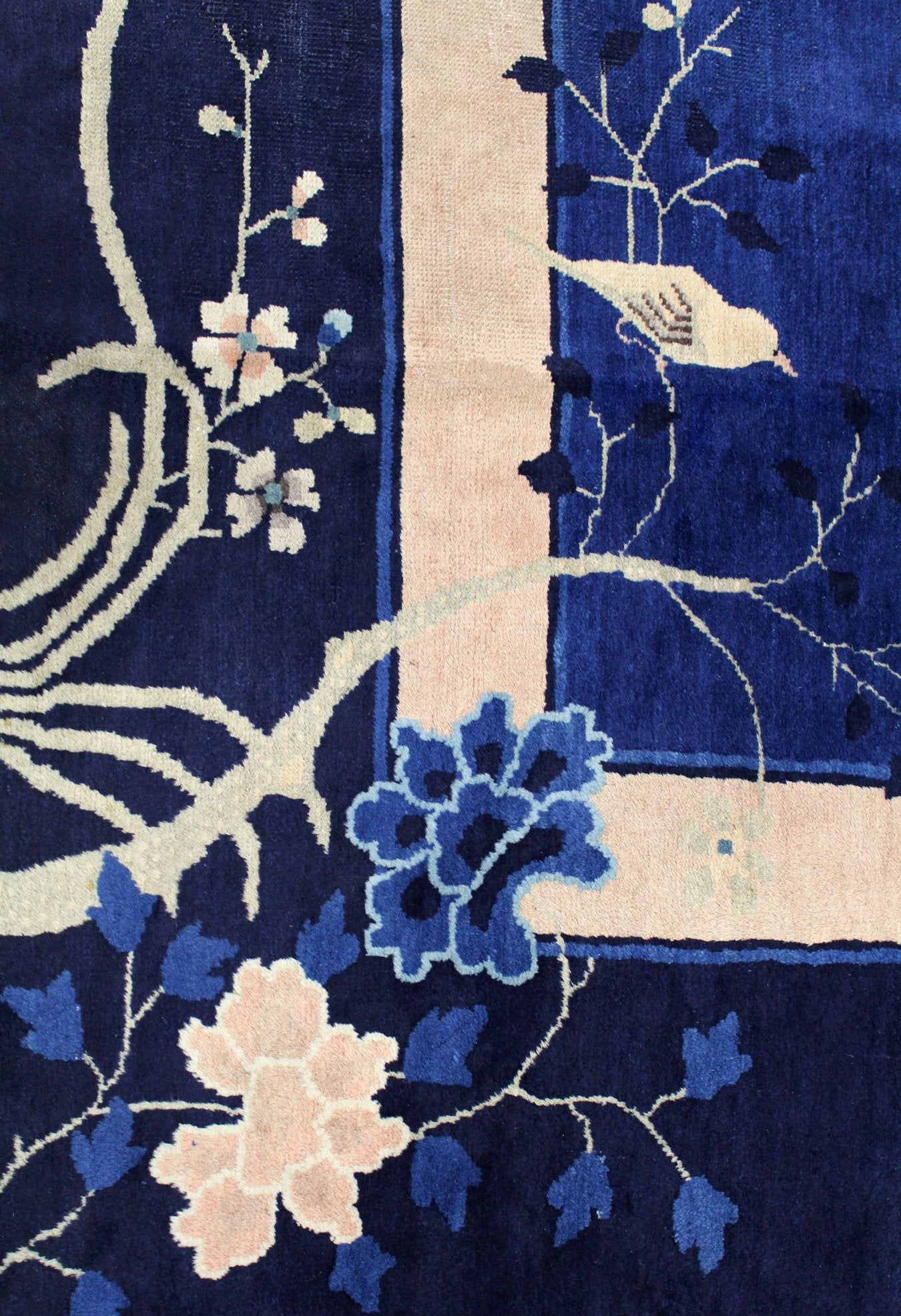 Detail of antique Peking rug; navy blue with handwoven floral and bird motifs, cream and blue accents.
