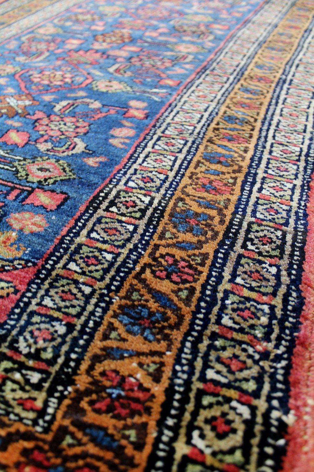 Close-up of antique handwoven rug detail, showcasing vibrant blue, orange, and red patterns.
