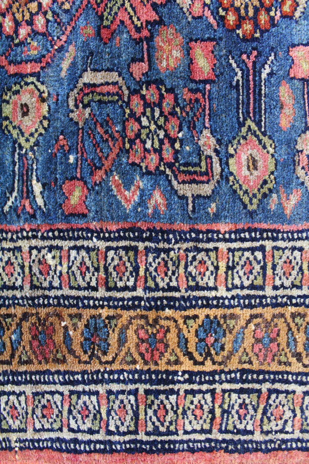 Detail of antique handwoven rug, showcasing intricate floral and geometric patterns in blue, red, and gold hues.
