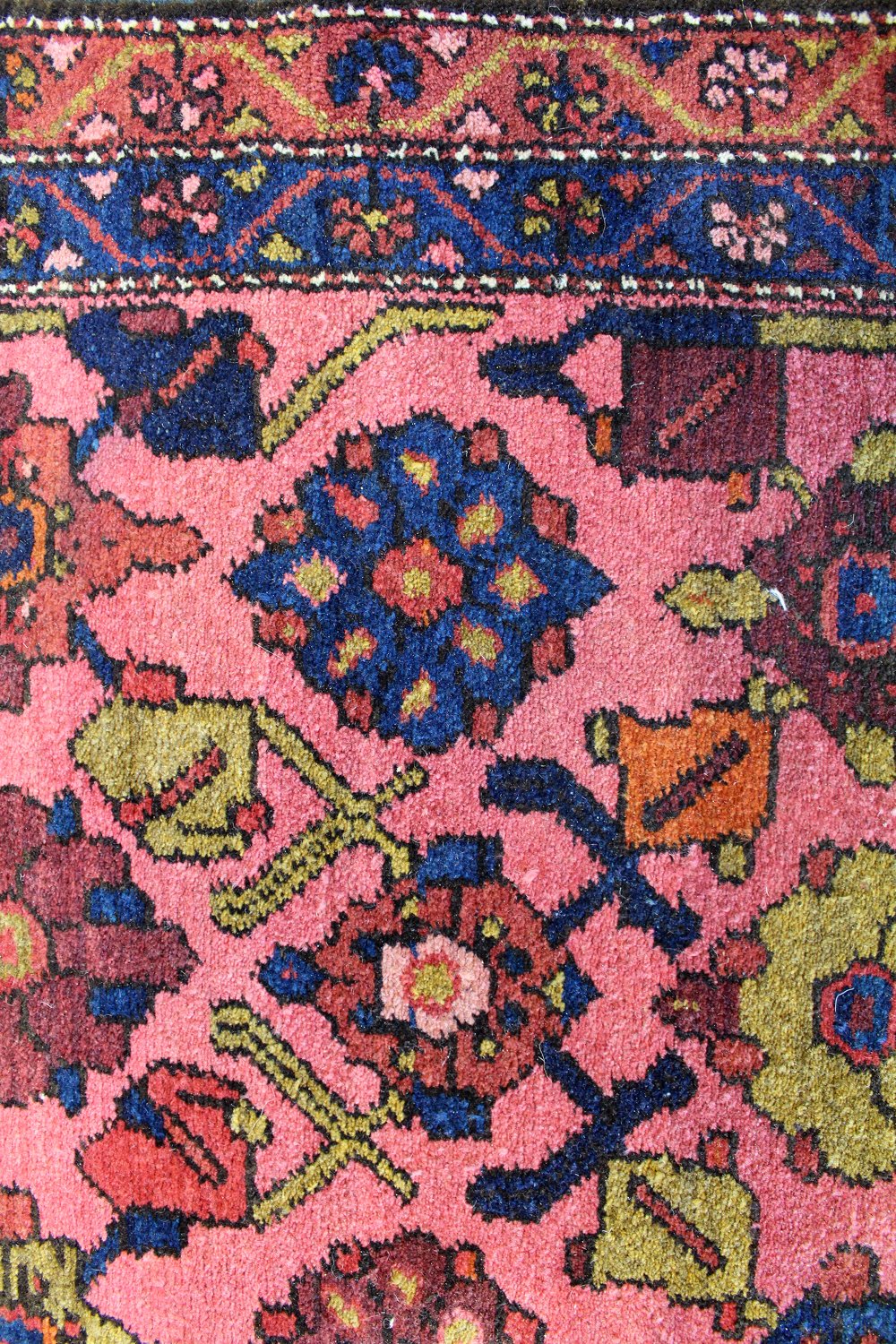 Detailed close-up of a pink antique Hamadan rug with intricate floral and geometric patterns in navy, gold, and red.
