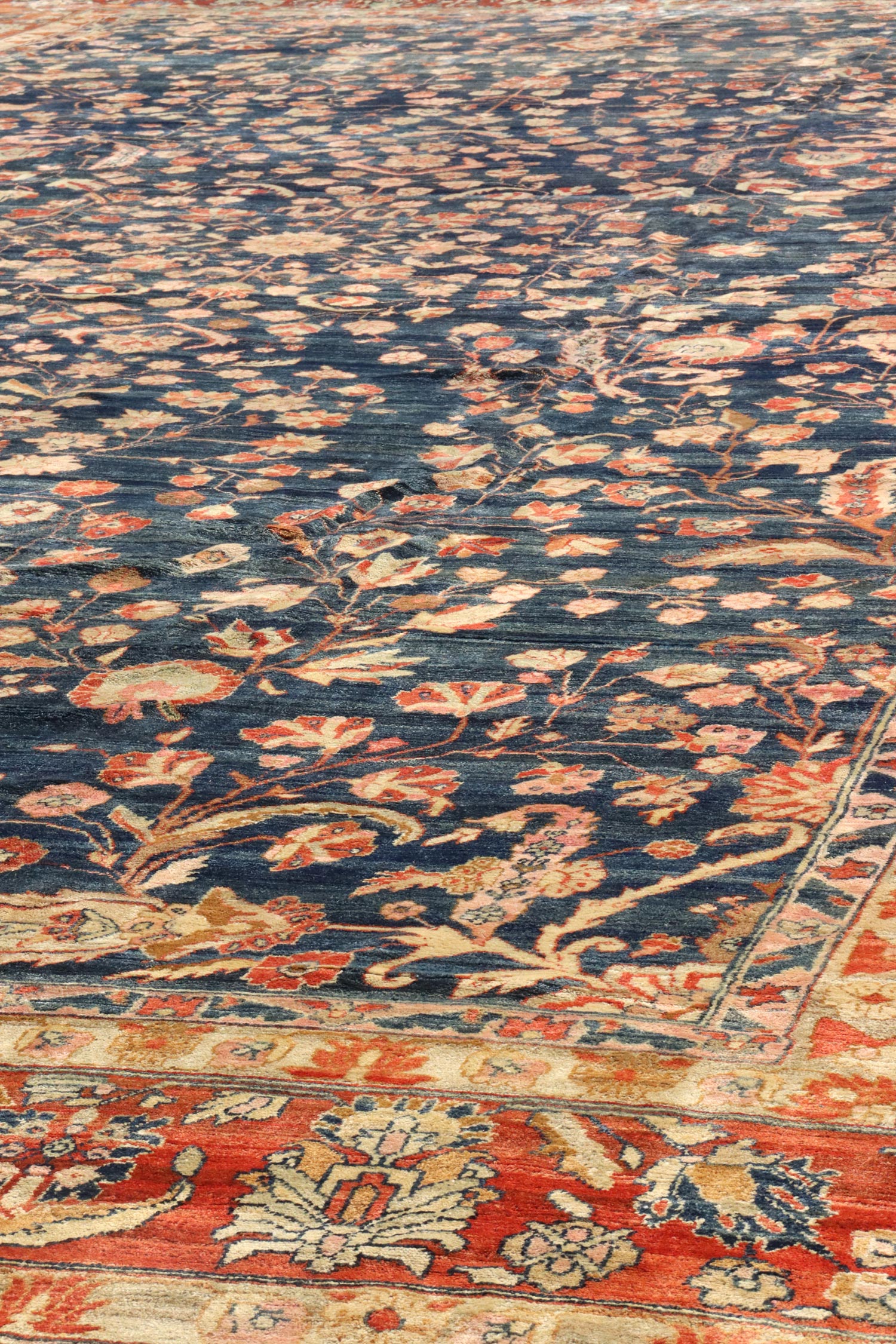 Handwoven antique rug with a navy blue field and a floral pattern in shades of orange and beige.
