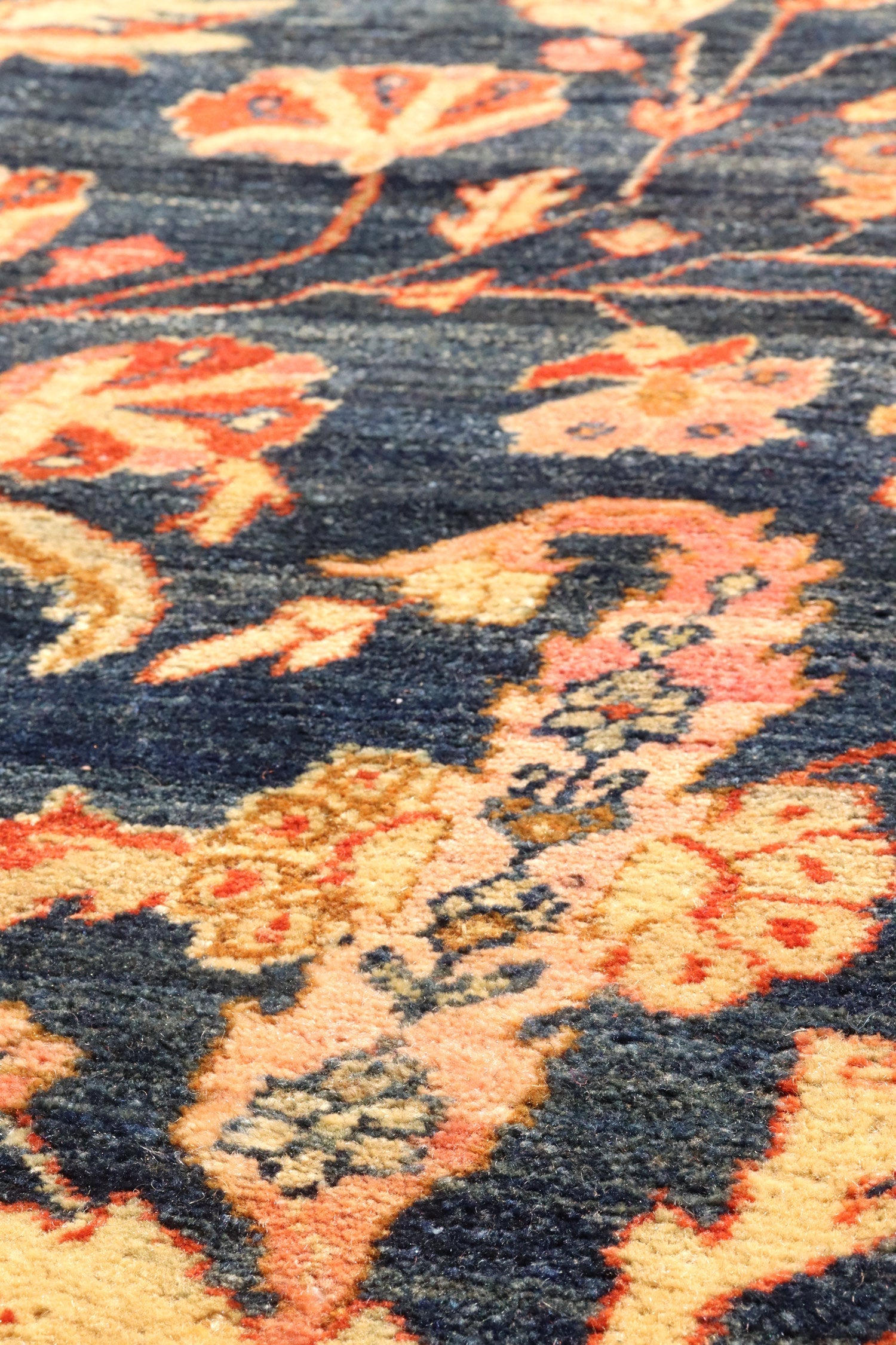 Close-up detail of a handwoven rug, showcasing its intricate floral pattern in shades of blue, orange, and beige.
