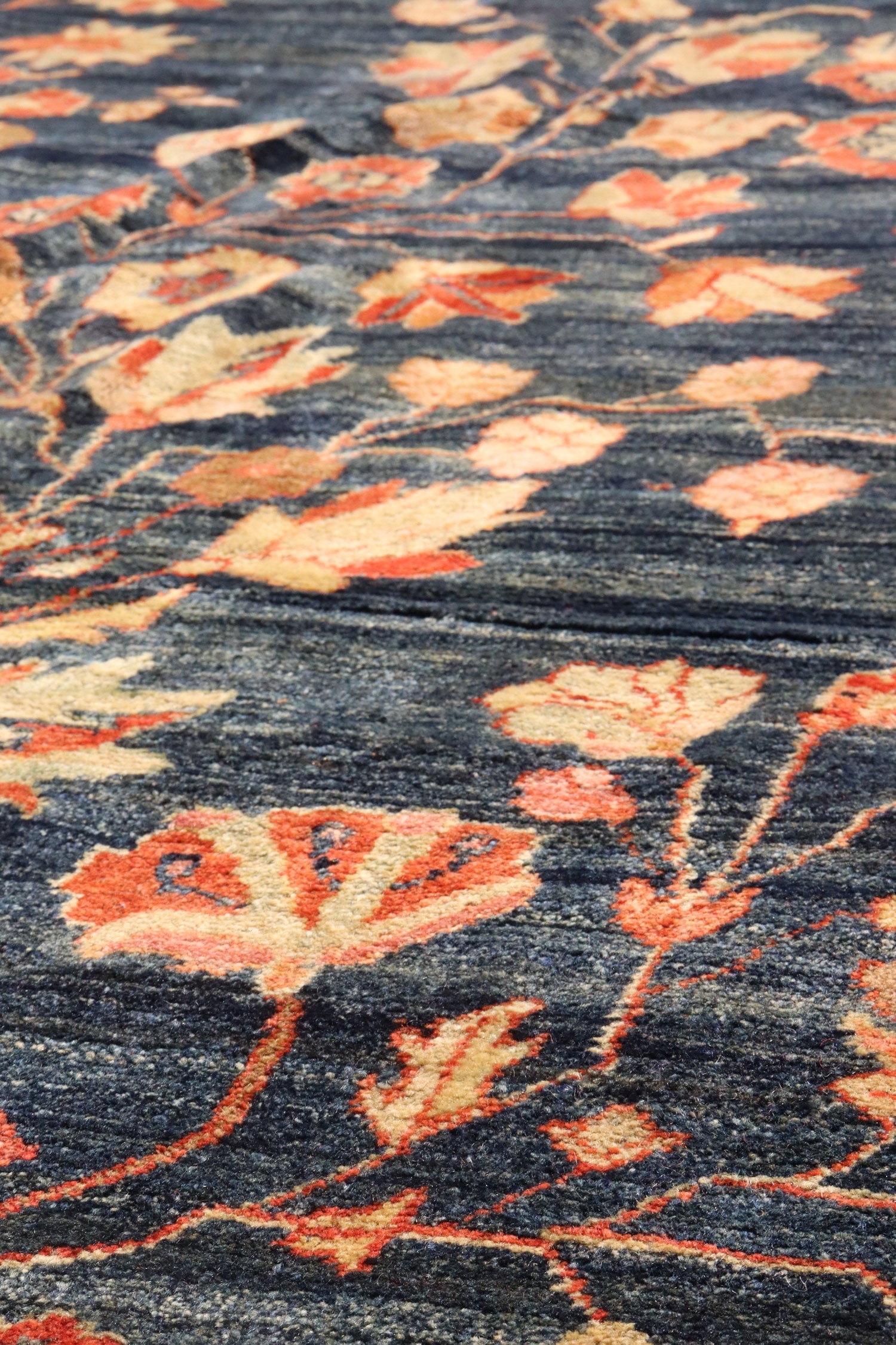 Close-up of a dark blue handwoven rug with a floral pattern in shades of orange and beige.
