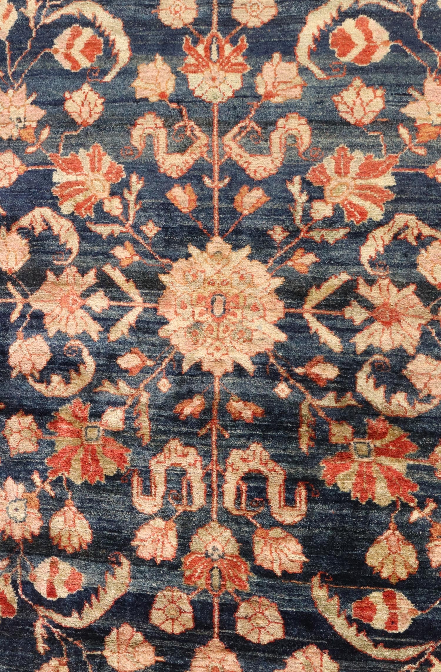 Close-up of antique rug's handwoven floral pattern in navy and coral.
