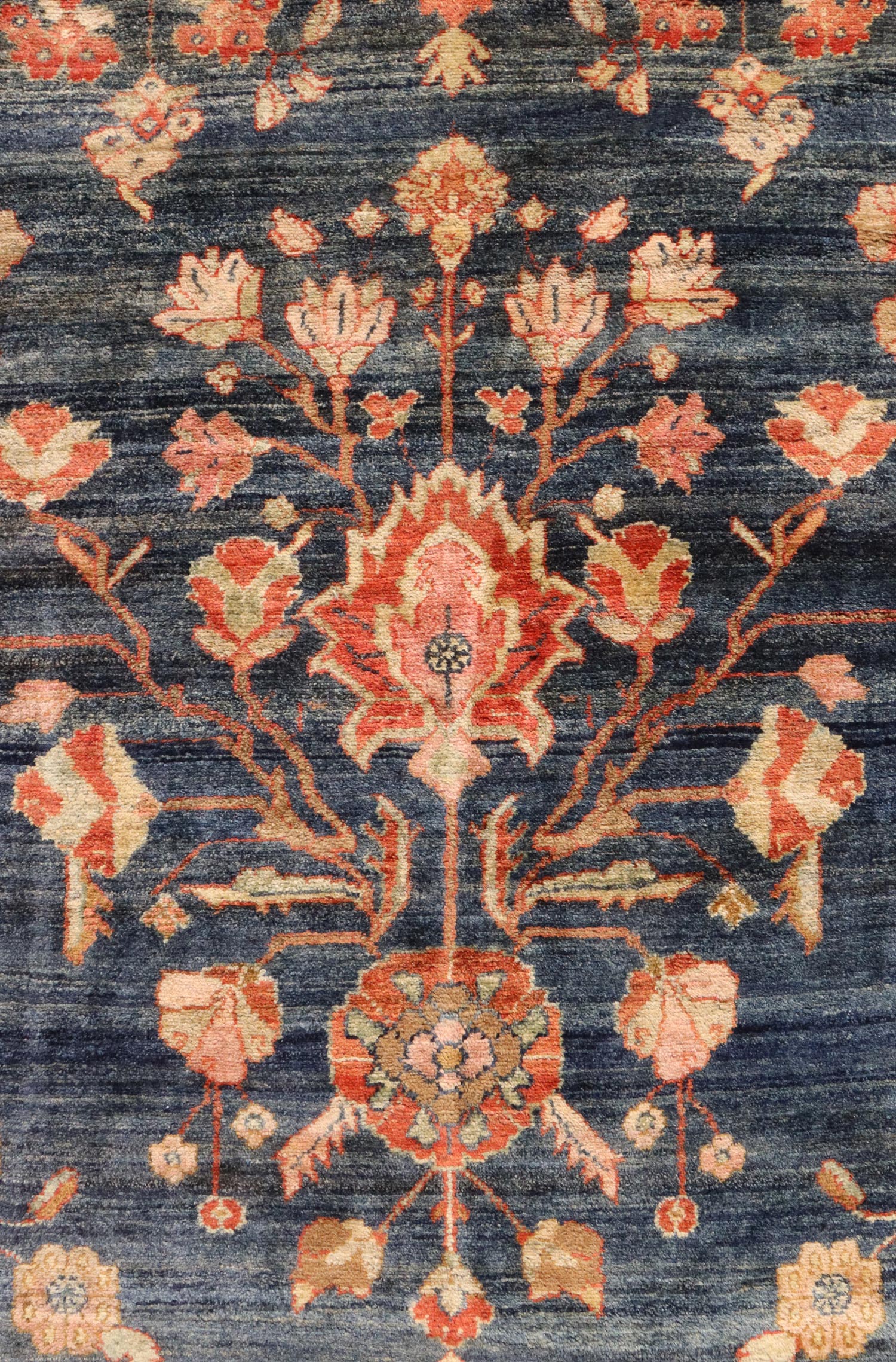 Handwoven rug detail:  Intricate floral pattern in muted reds and peaches on a deep blue background.
