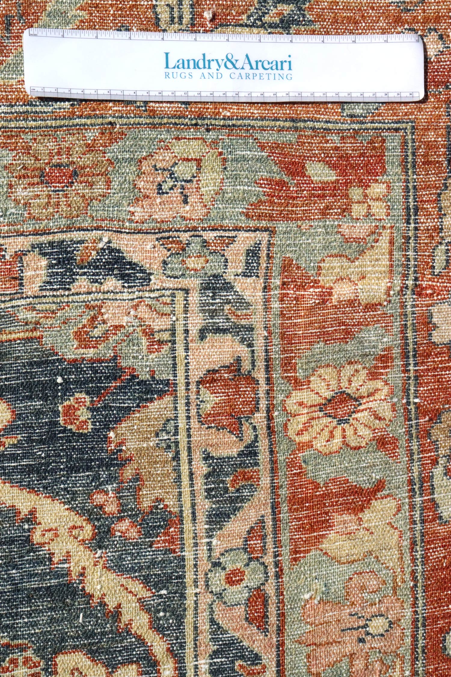 Detailed close-up of an antique rug's handwoven texture, showcasing muted reds, blues, and creams in a traditional floral pattern.
