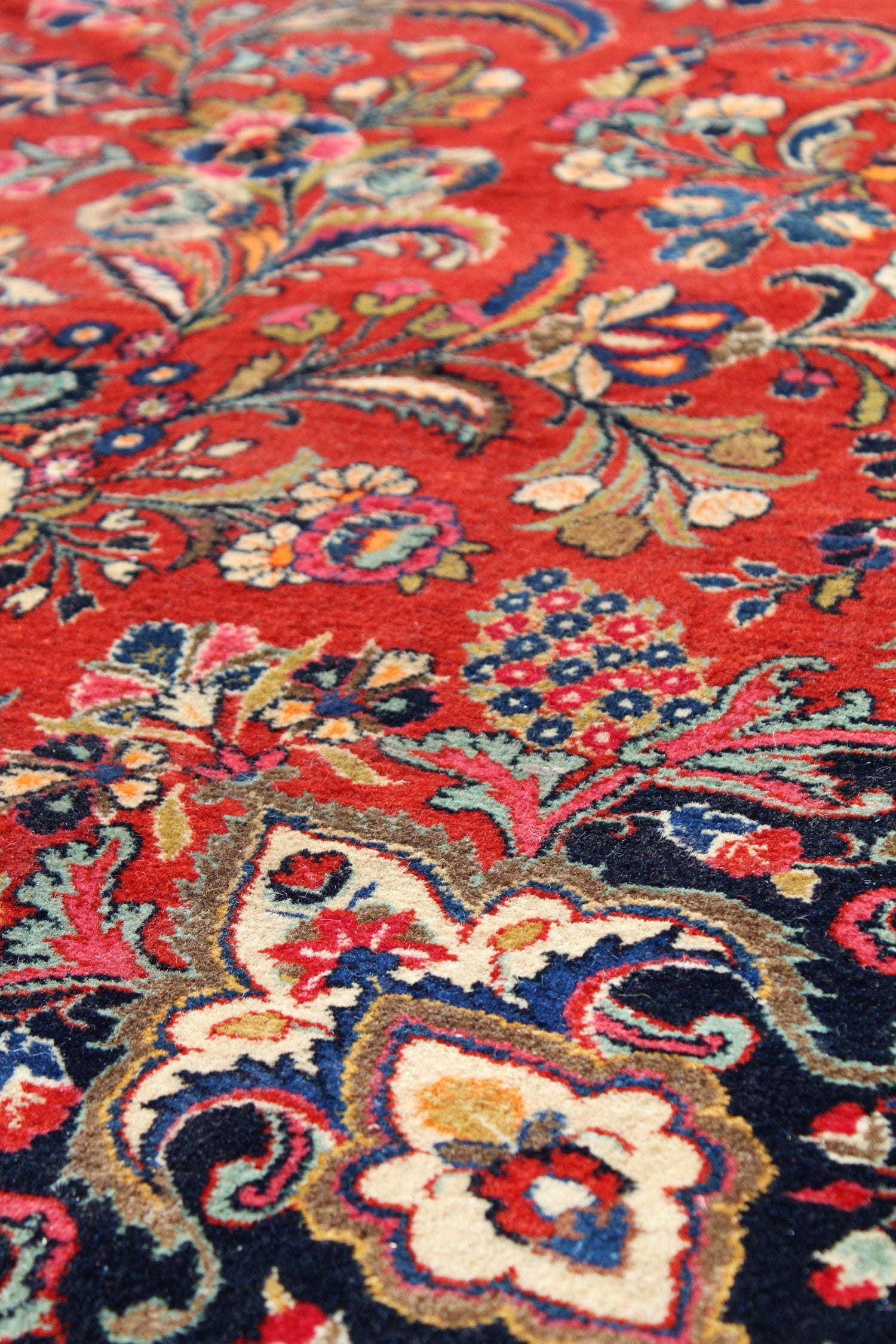 Close-up of a richly colored antique rug, showcasing intricate floral patterns in red, blue, and cream.
