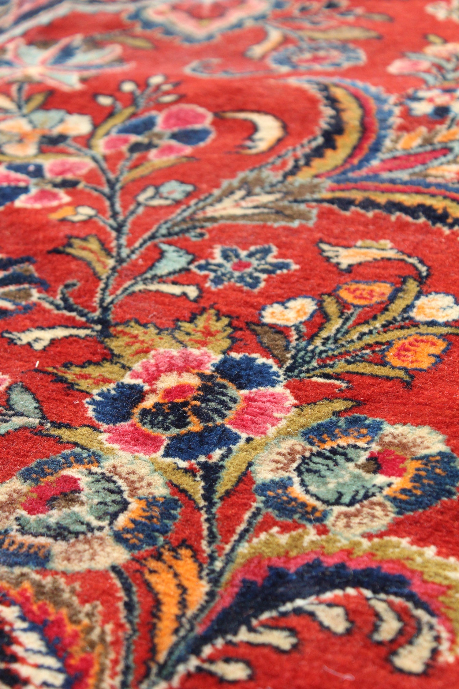 Close-up of a handwoven rug's vibrant floral pattern in rich reds, blues, and greens.
