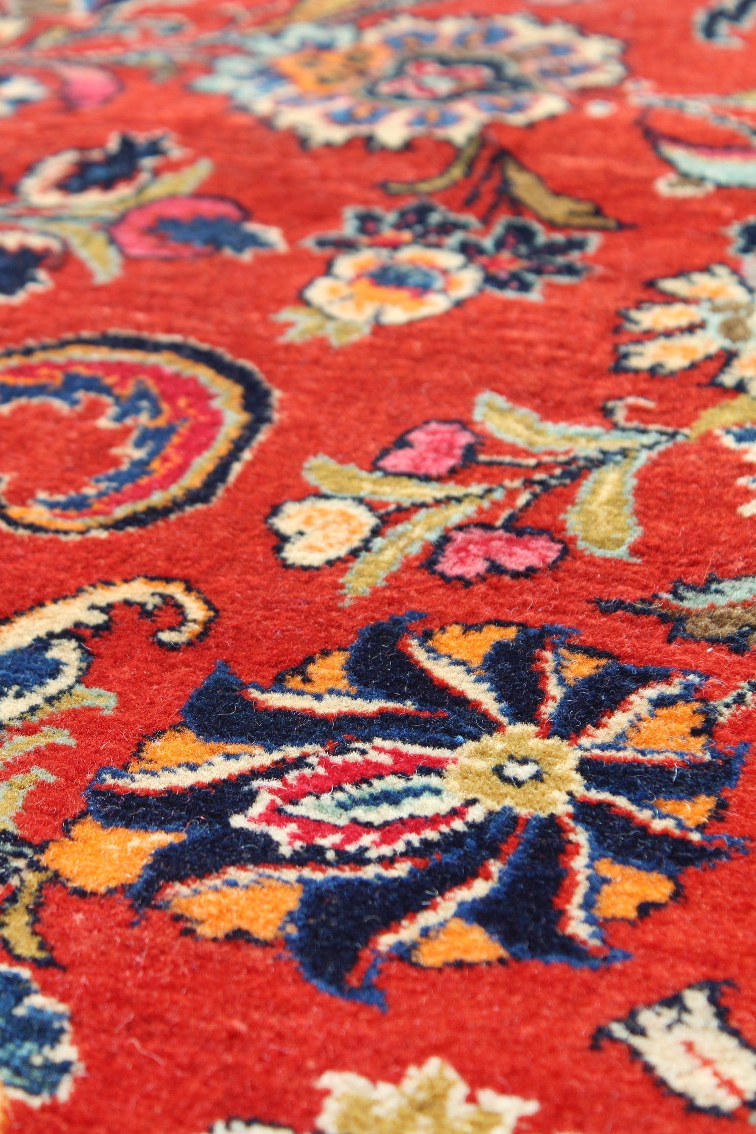 Close-up of a red handwoven rug with intricate floral details in navy, gold, and cream.
