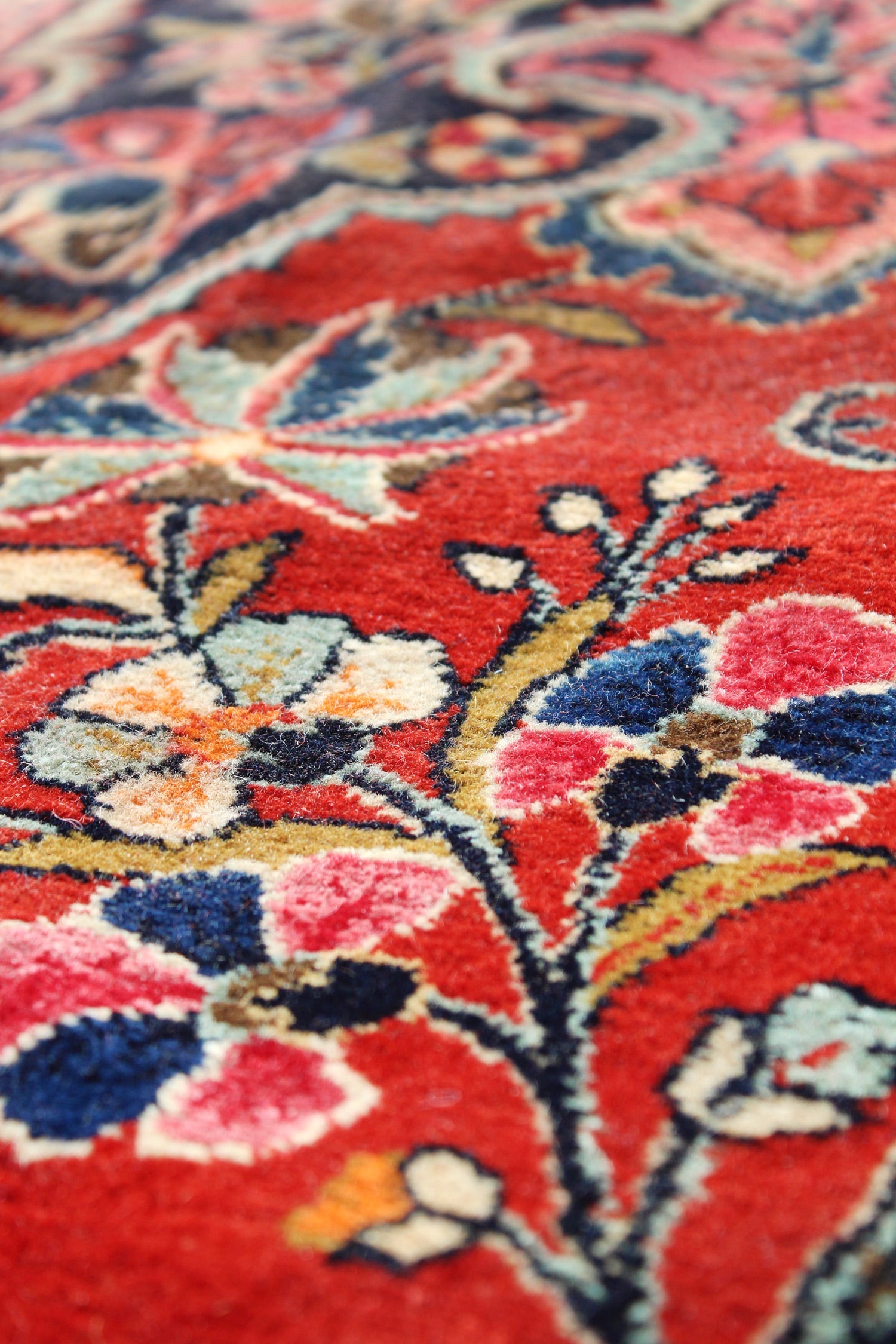 Close-up of handwoven rug detail, showcasing vibrant floral pattern in red, blue, and cream tones.
