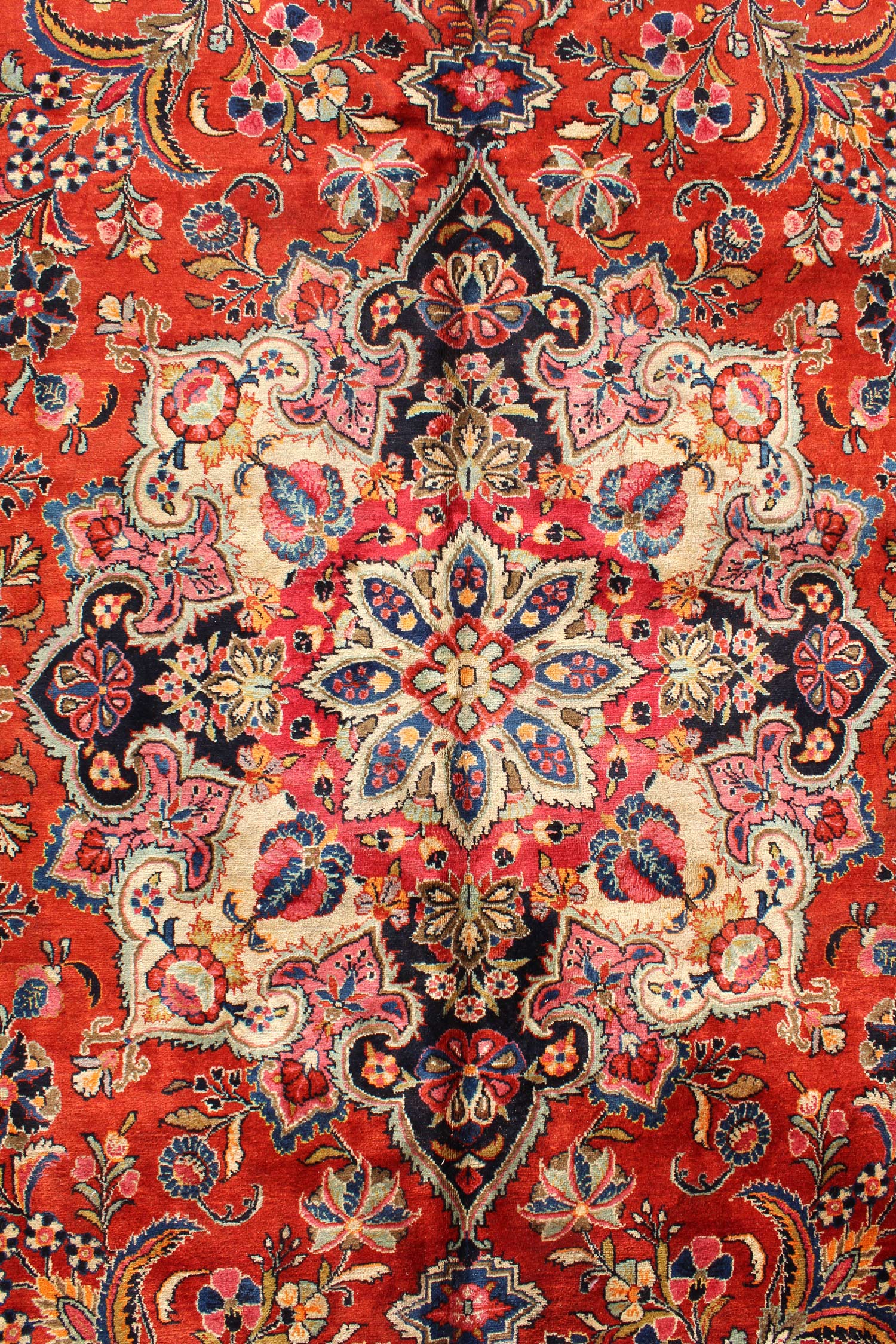 Intricate detail of a traditional handwoven rug, showcasing a vibrant red base with a central medallion of multicolored floral patterns.
