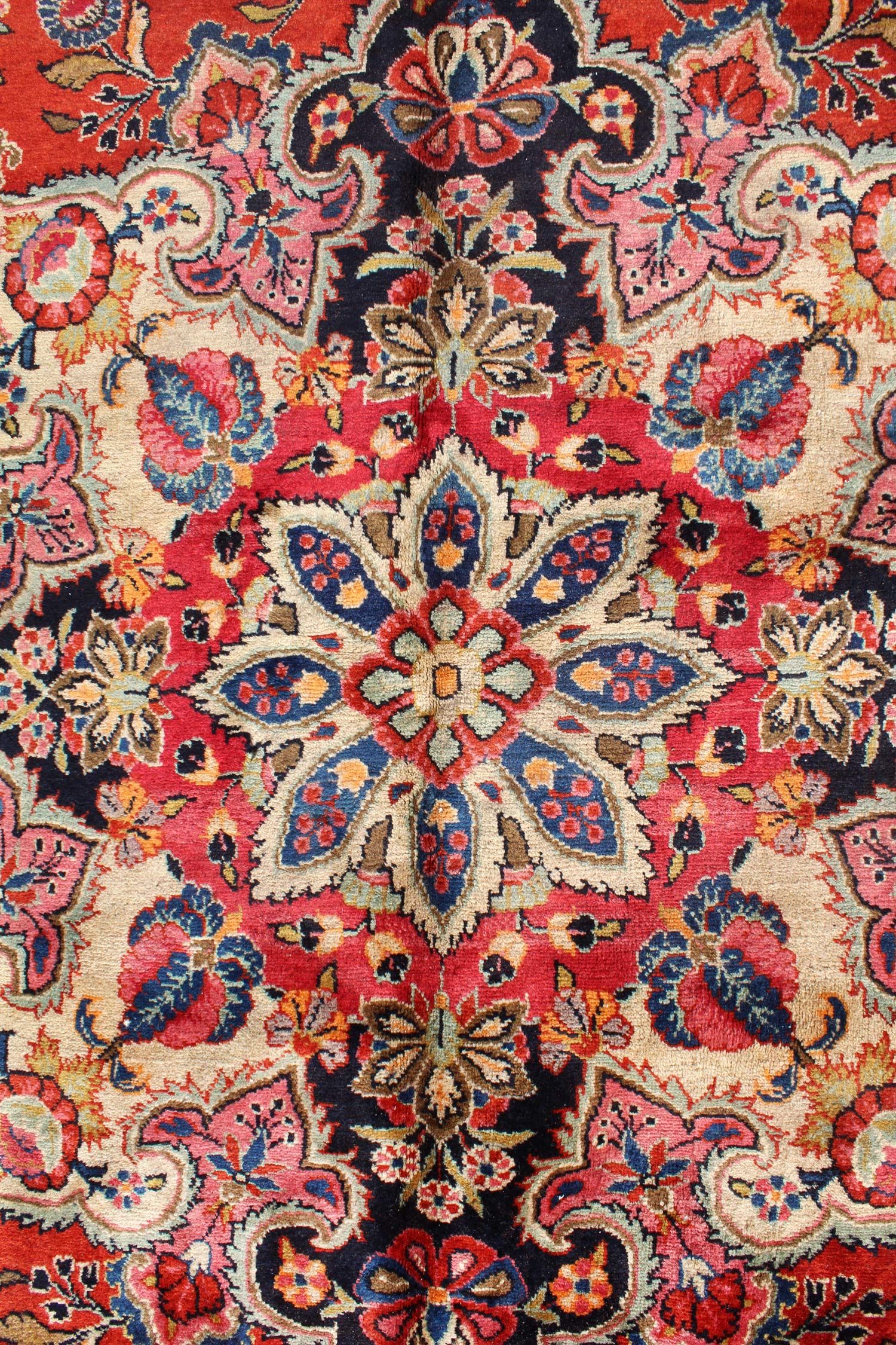 Detail of antique Ekbatan rug, showcasing vibrant floral patterns in red, blue, and cream.
