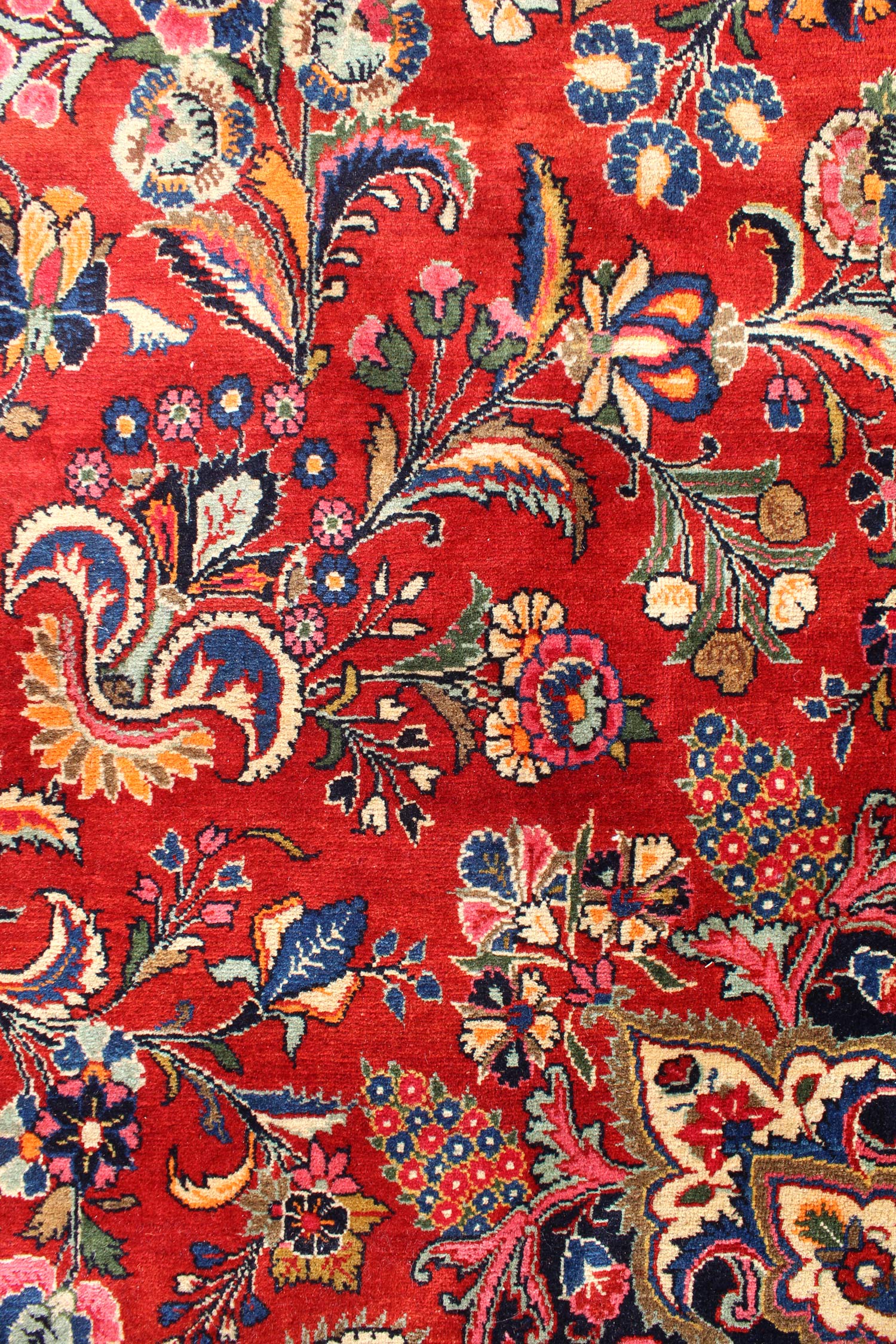 Intricate floral detail on a red antique rug, showcasing a traditional handwoven design.
