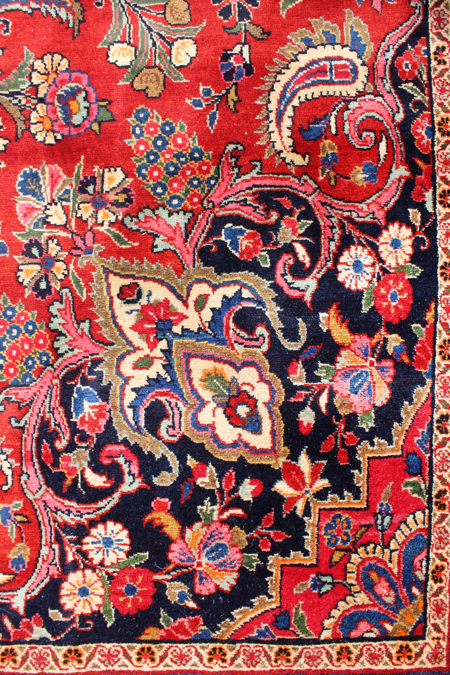 Detail of an antique Ekbatan rug, showcasing its intricate floral and paisley patterns in rich reds, blues, and creams.
