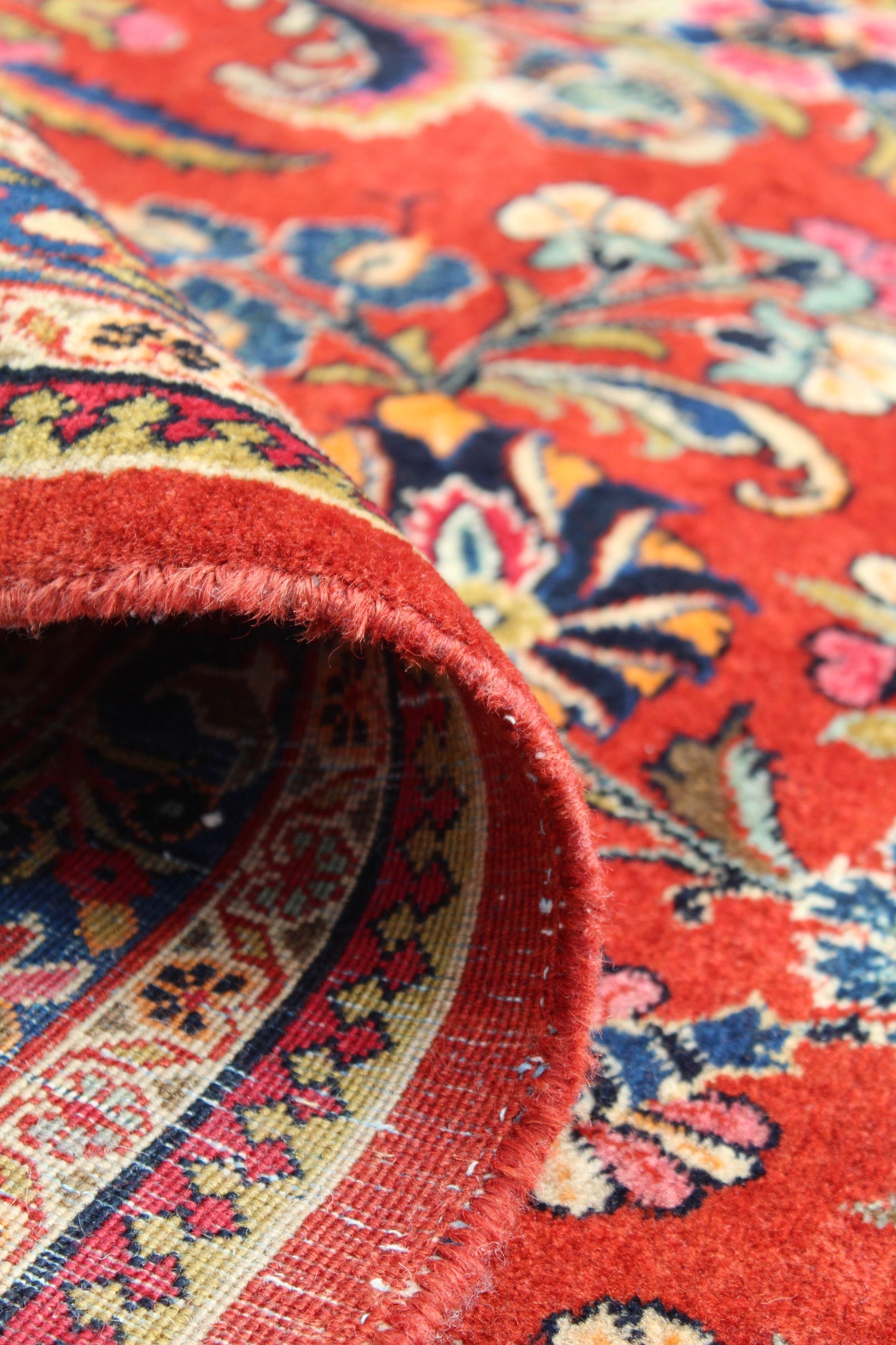 Close-up of antique rug's edge, showcasing intricate handwoven details and rich red tones.
