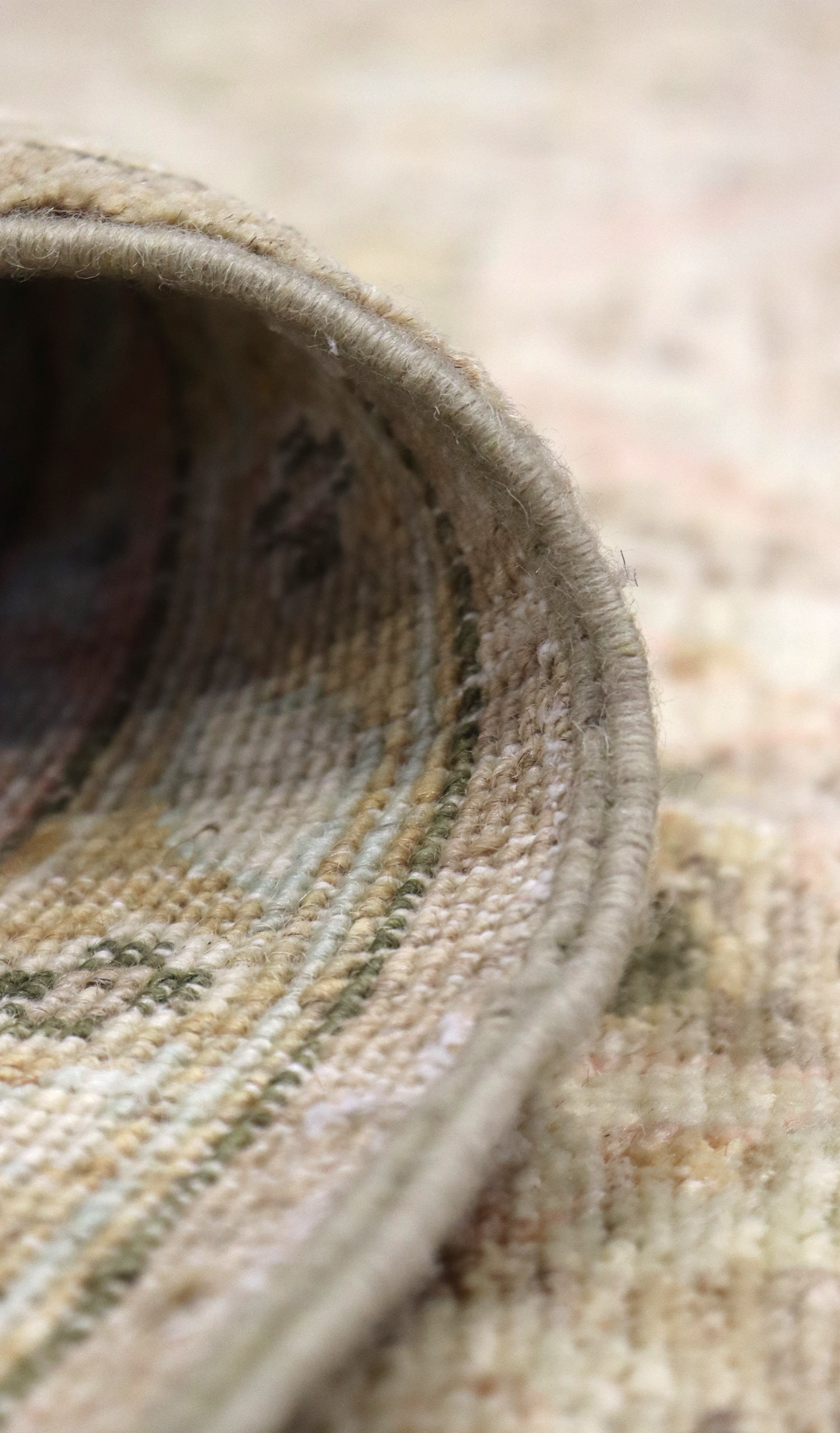 Close-up of handwoven rug edge, showcasing beige and green tones in detailed texture.
