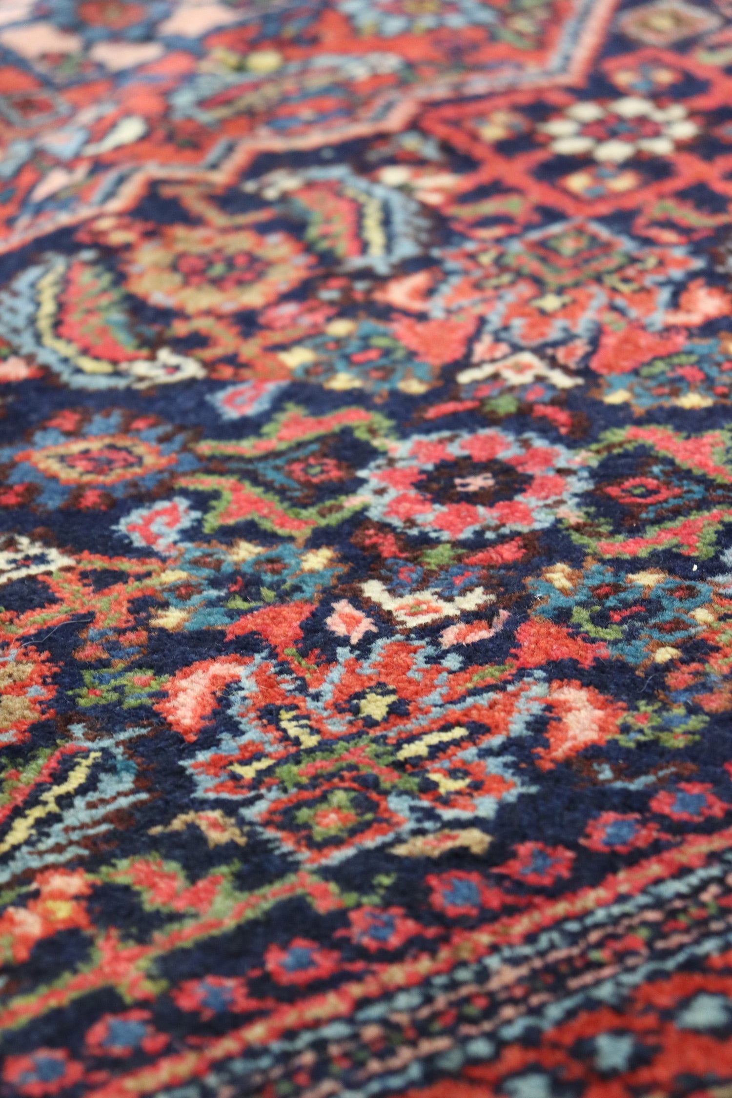 Close-up of a richly colored handwoven rug, showcasing intricate tribal patterns in reds, blues, and greens.
