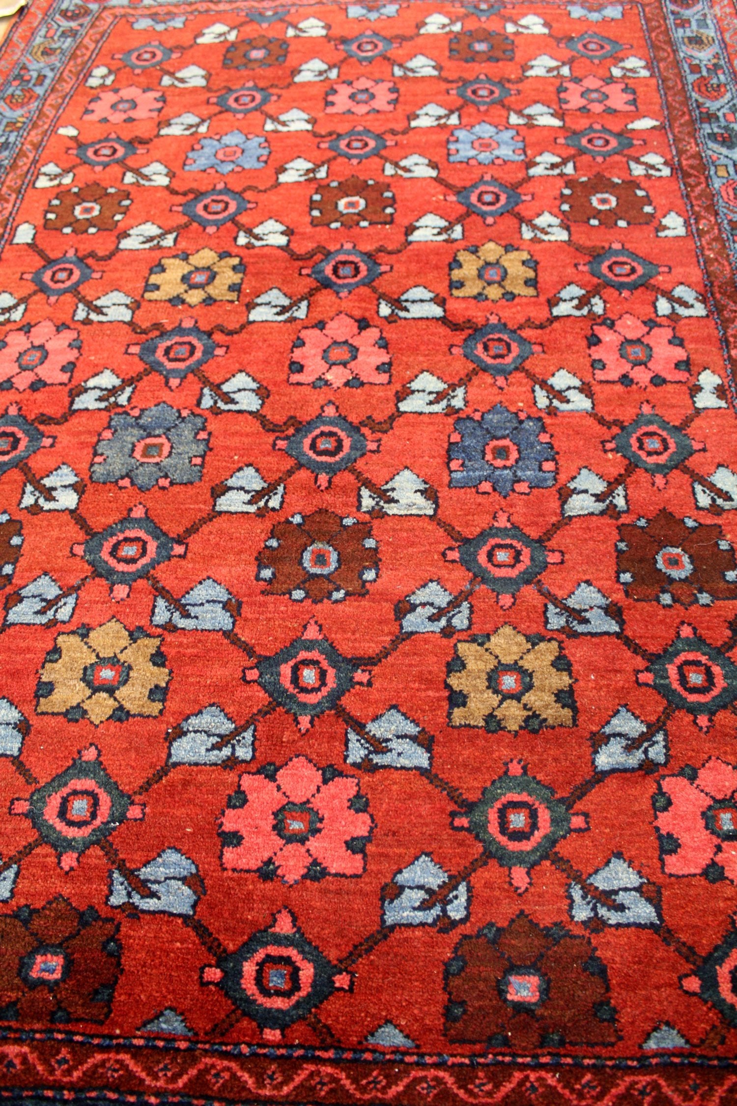 Handwoven rug detail, showcasing a red base with intricate blue, brown, and pink floral patterns.
