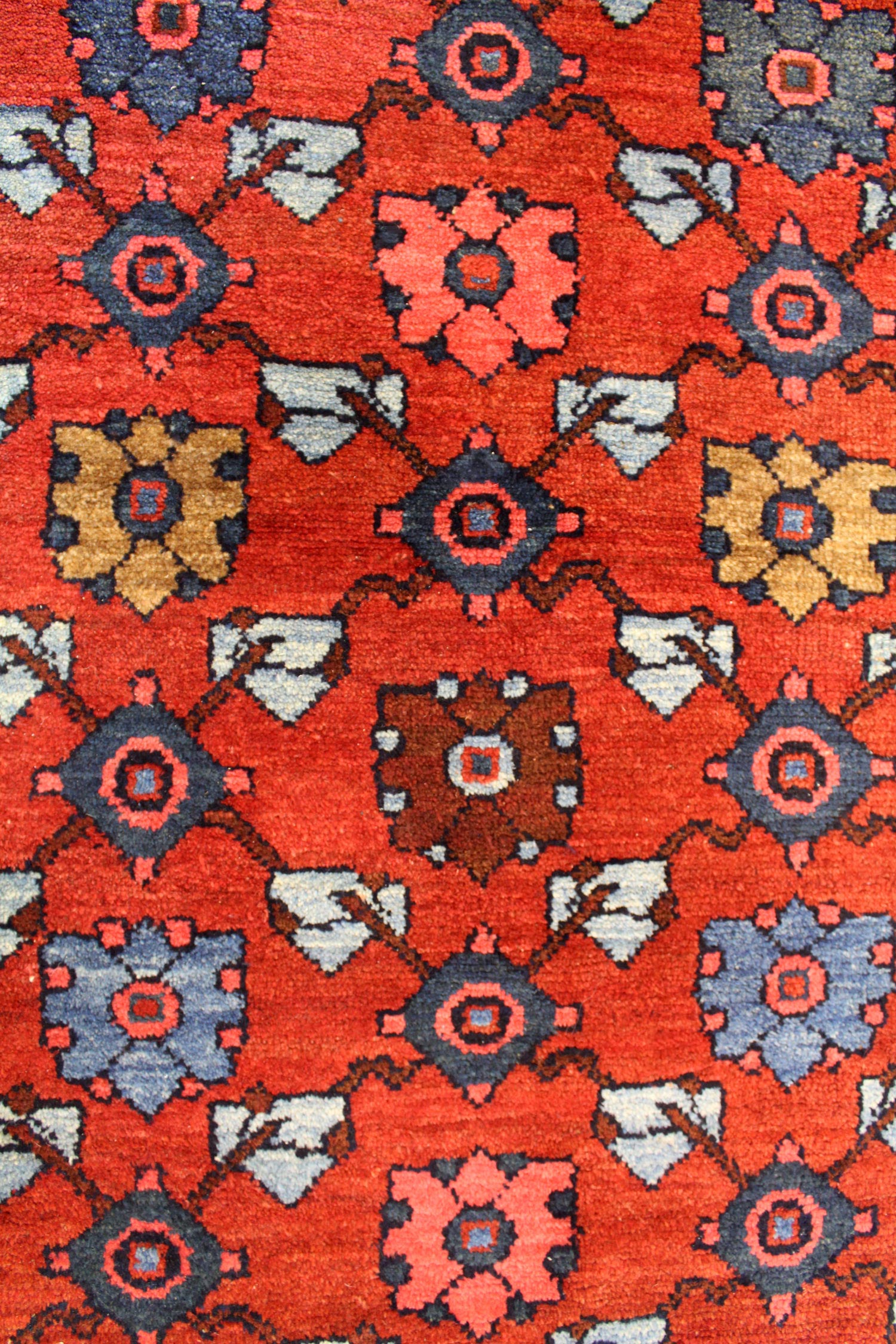 Detail of a handwoven rug's vibrant red base with geometric floral patterns in blue, pink, and brown.
